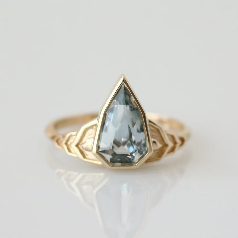 A gold ring with a large, clear, pointed gemstone in the center and a decorative band.