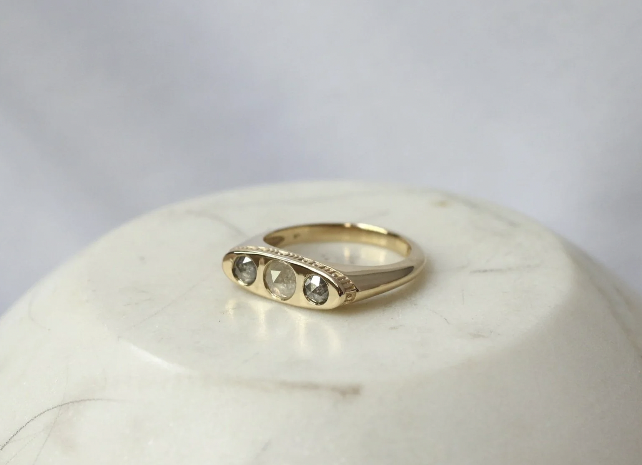 Gold ring with three embedded gemstones placed on a white surface.