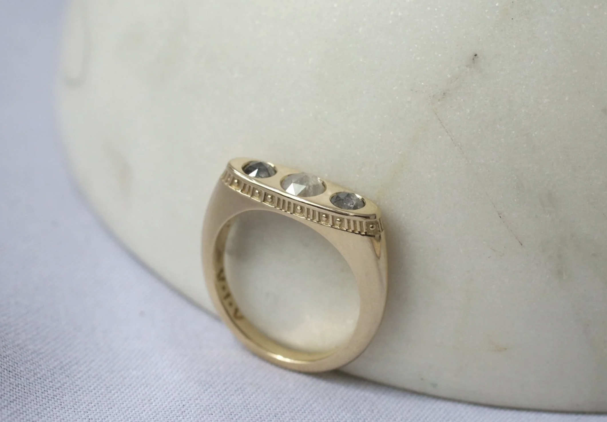 Gold ring with three gemstones, placed on a white textured surface.