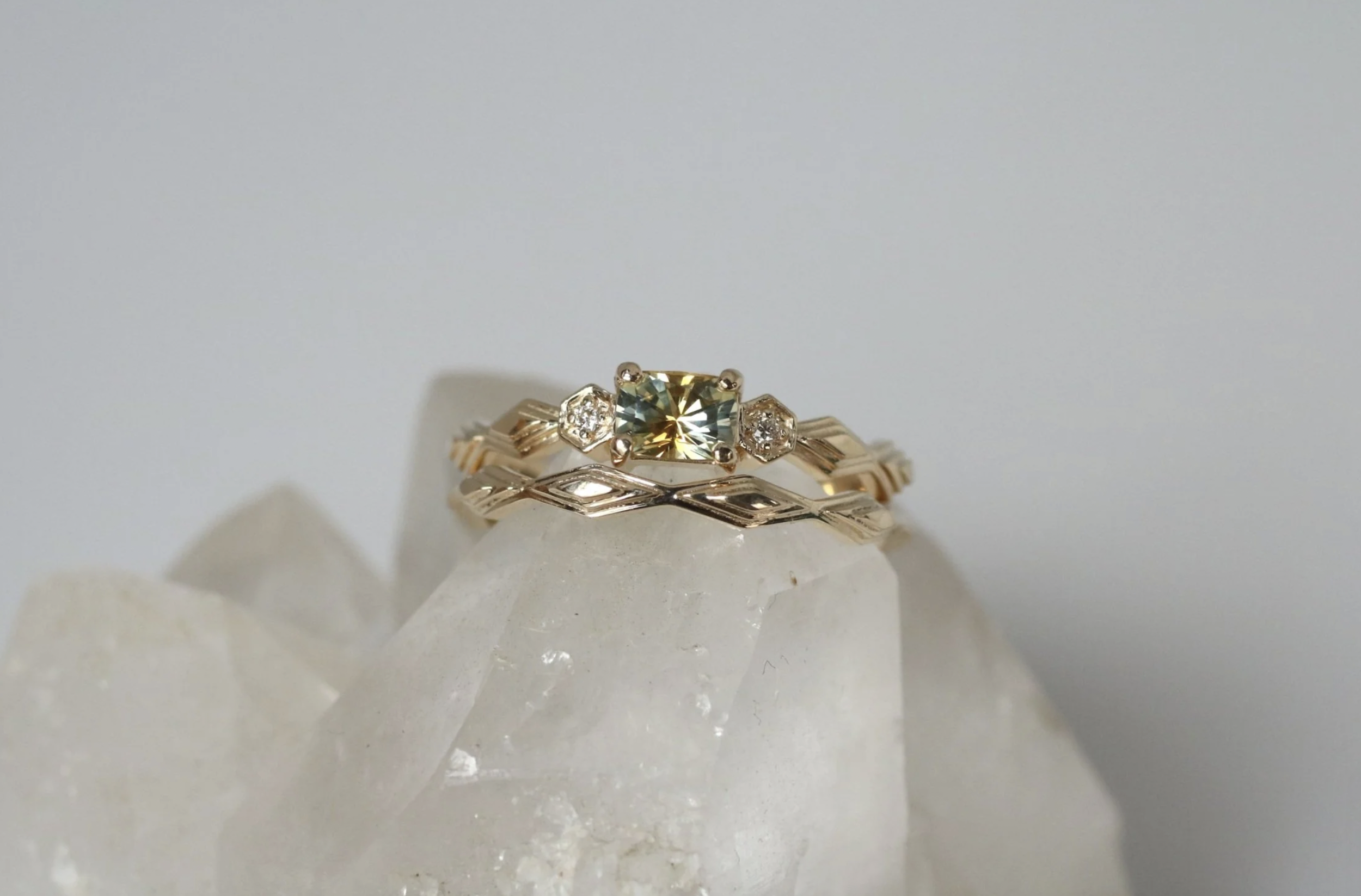 Gold rings with a central diamond and smaller diamonds on a translucent white stone with a plain white background.