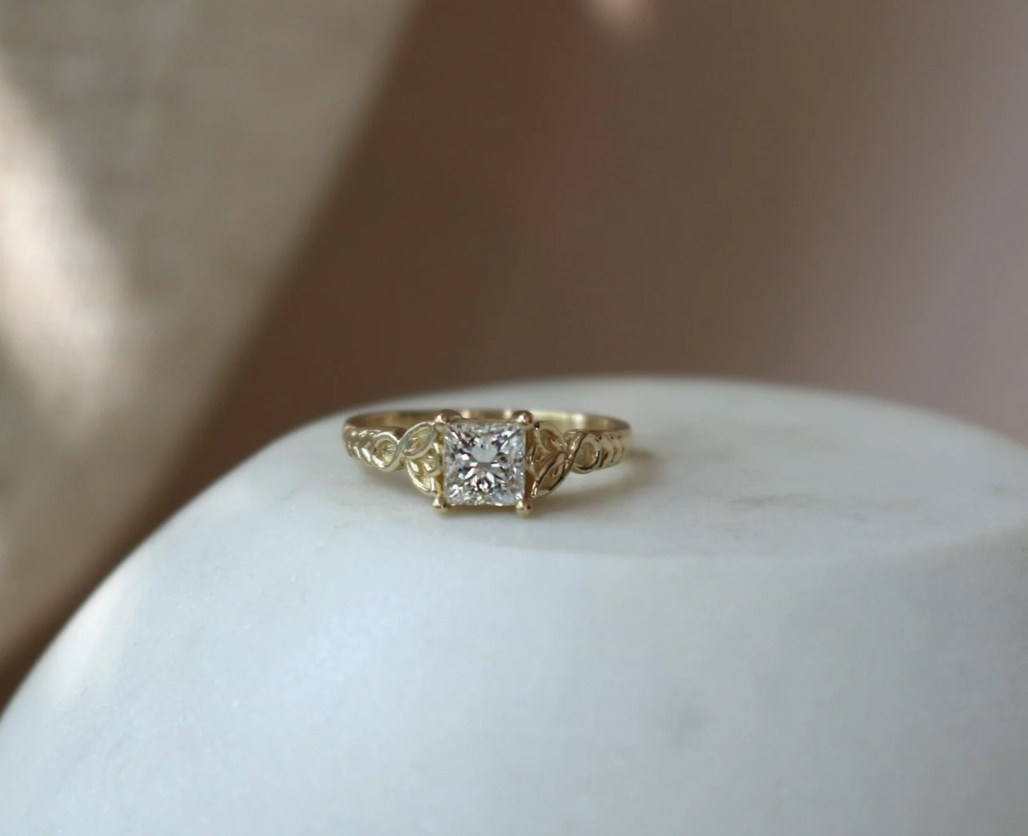 Gold engagement ring with a square diamond solitaire on a white surface