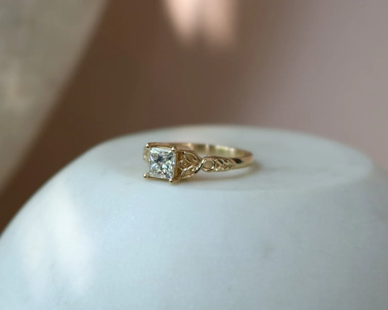 Gold ring with a square diamond on a white surface.