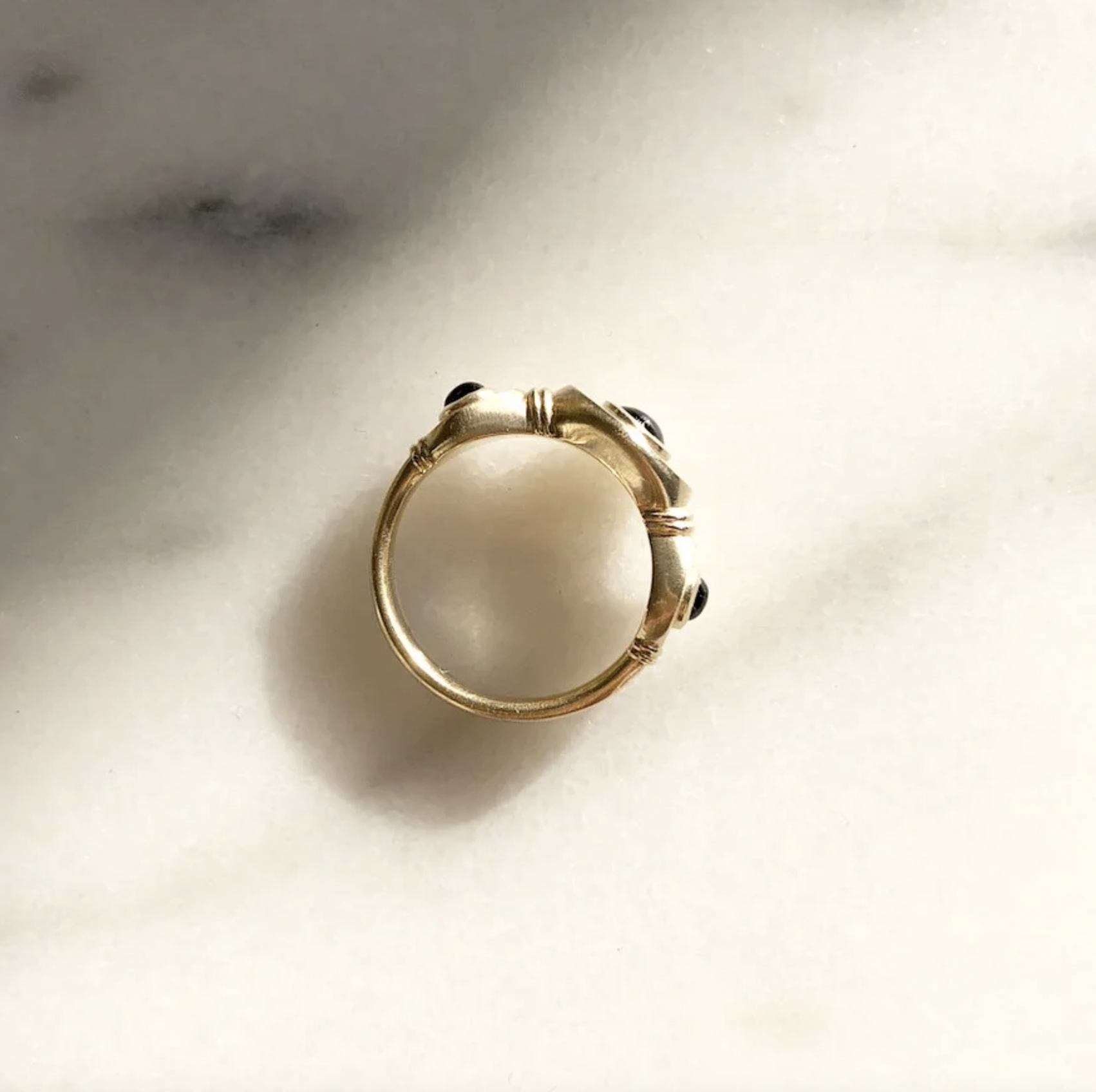 A gold ring with black gemstones resting on a white surface.