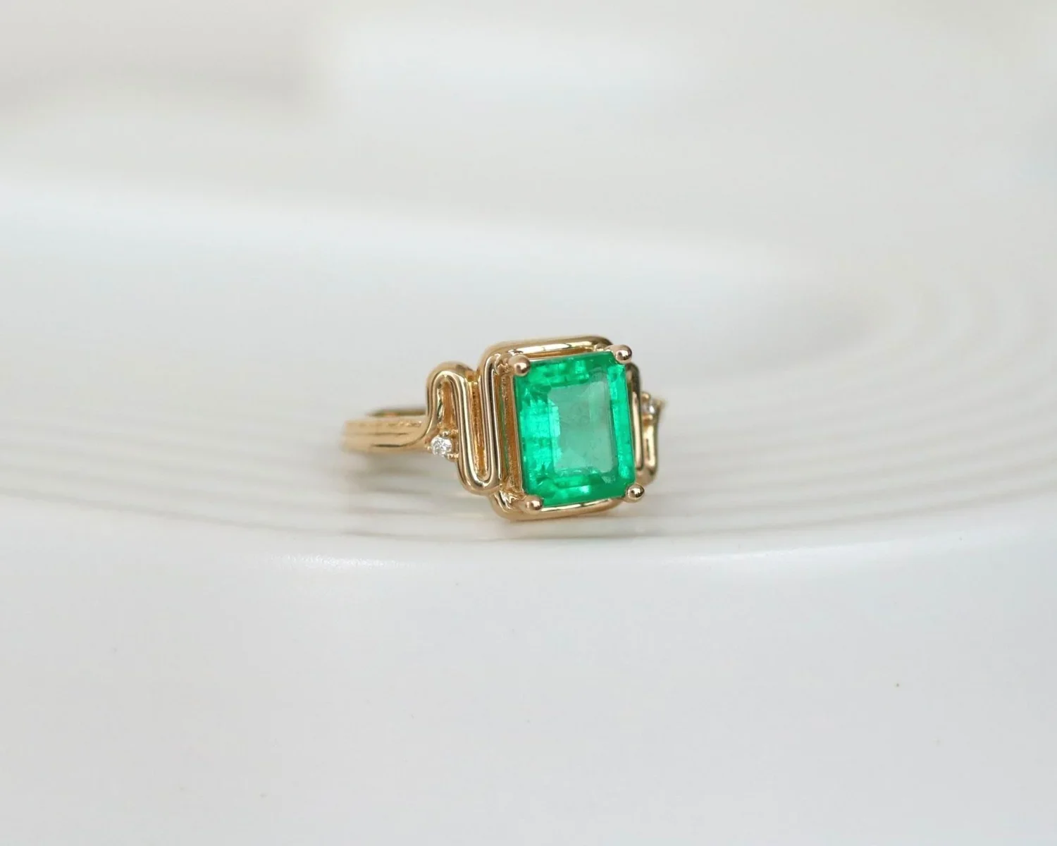 Gold ring with a large rectangular green gemstone and small diamonds on a white textured surface.