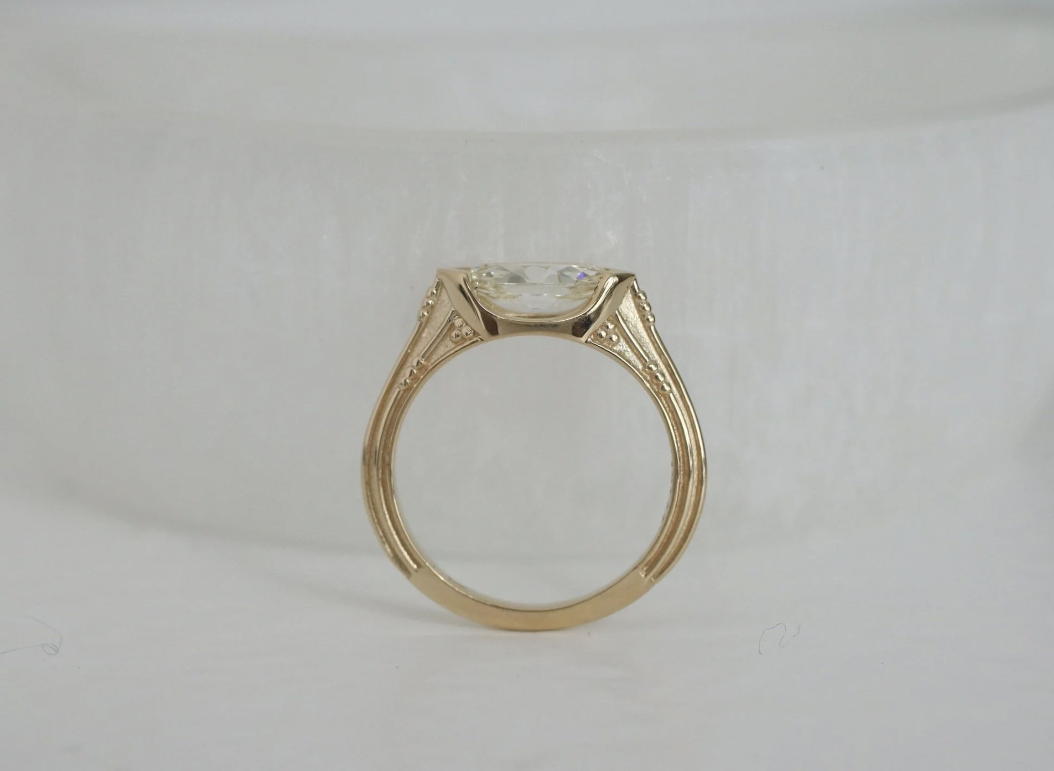 A gold ring with a large clear gemstone, viewed from the side against a plain background.