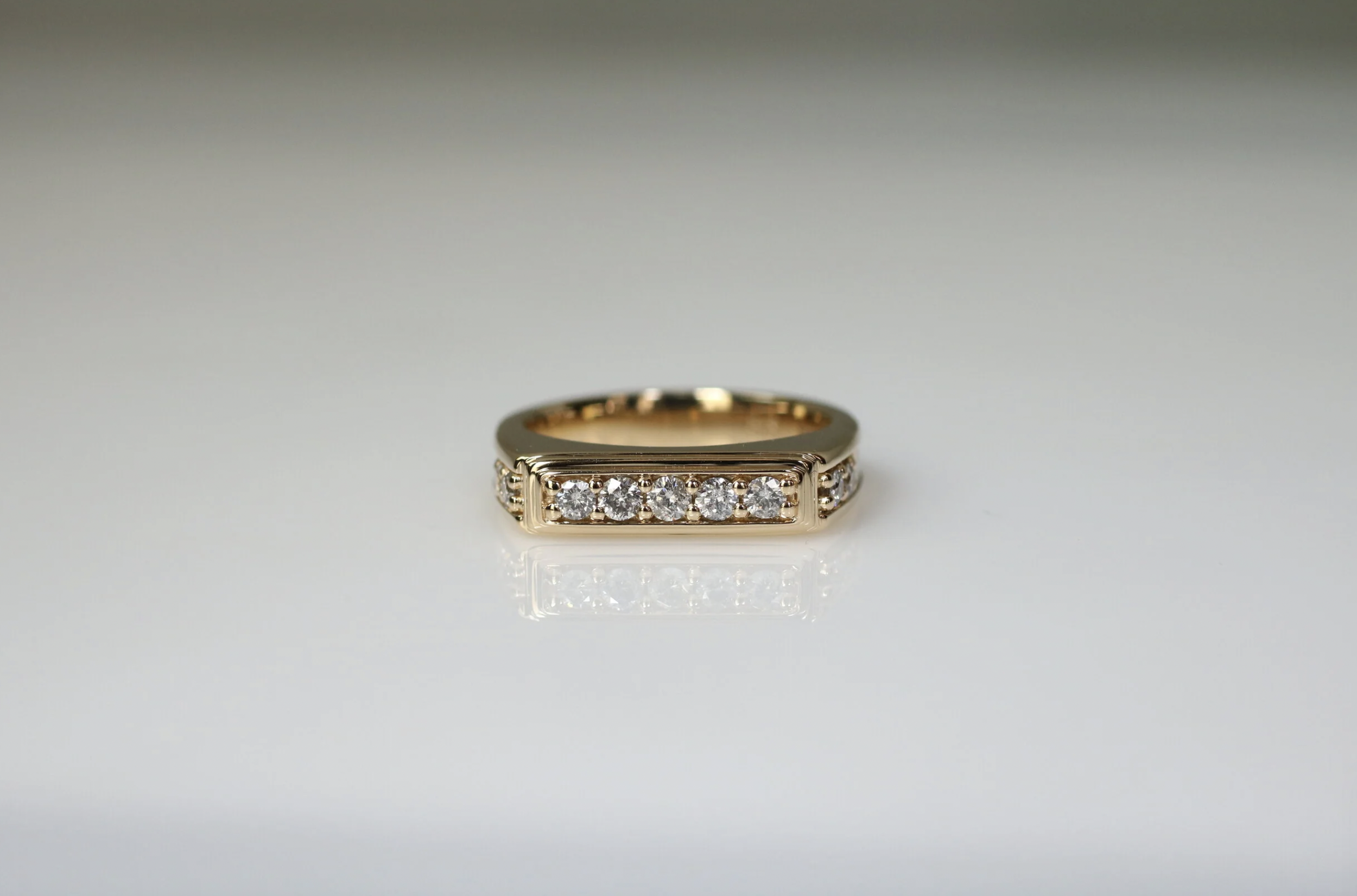 Gold ring with rectangular setting of five diamonds on a reflective surface