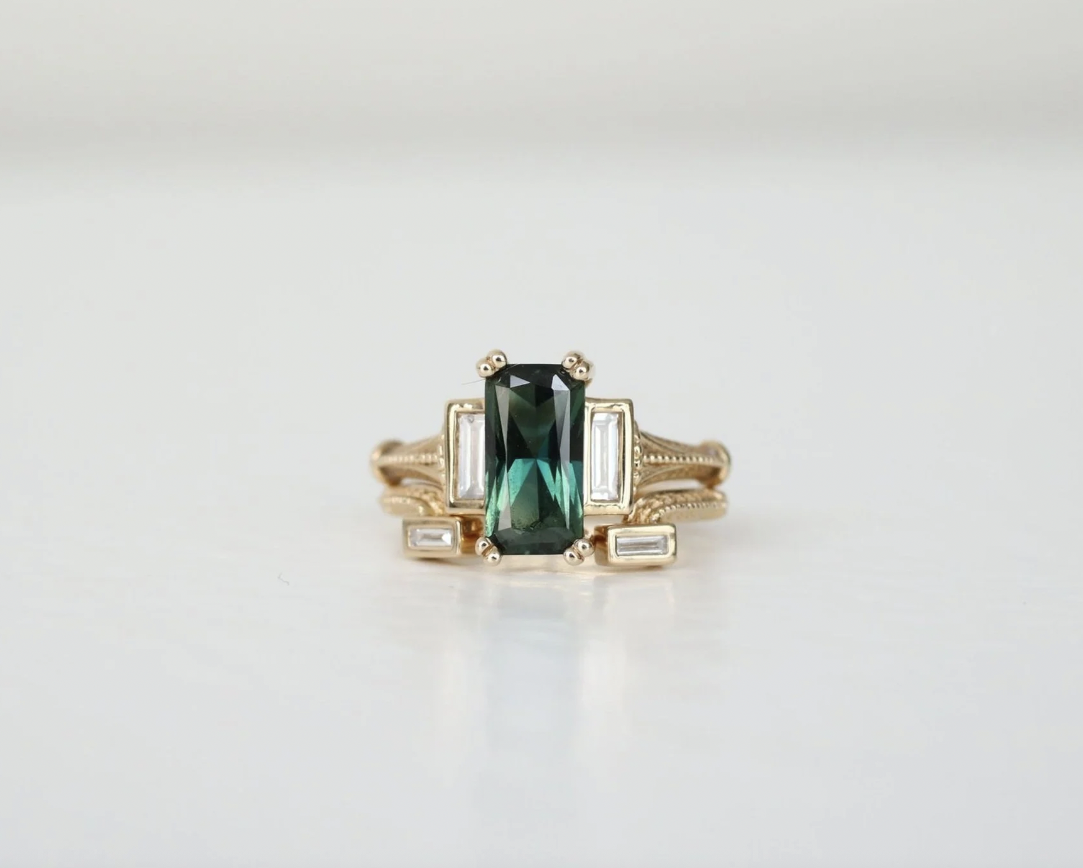 Gold ring with a rectangular dark green gemstone and small baguette diamonds on each side.