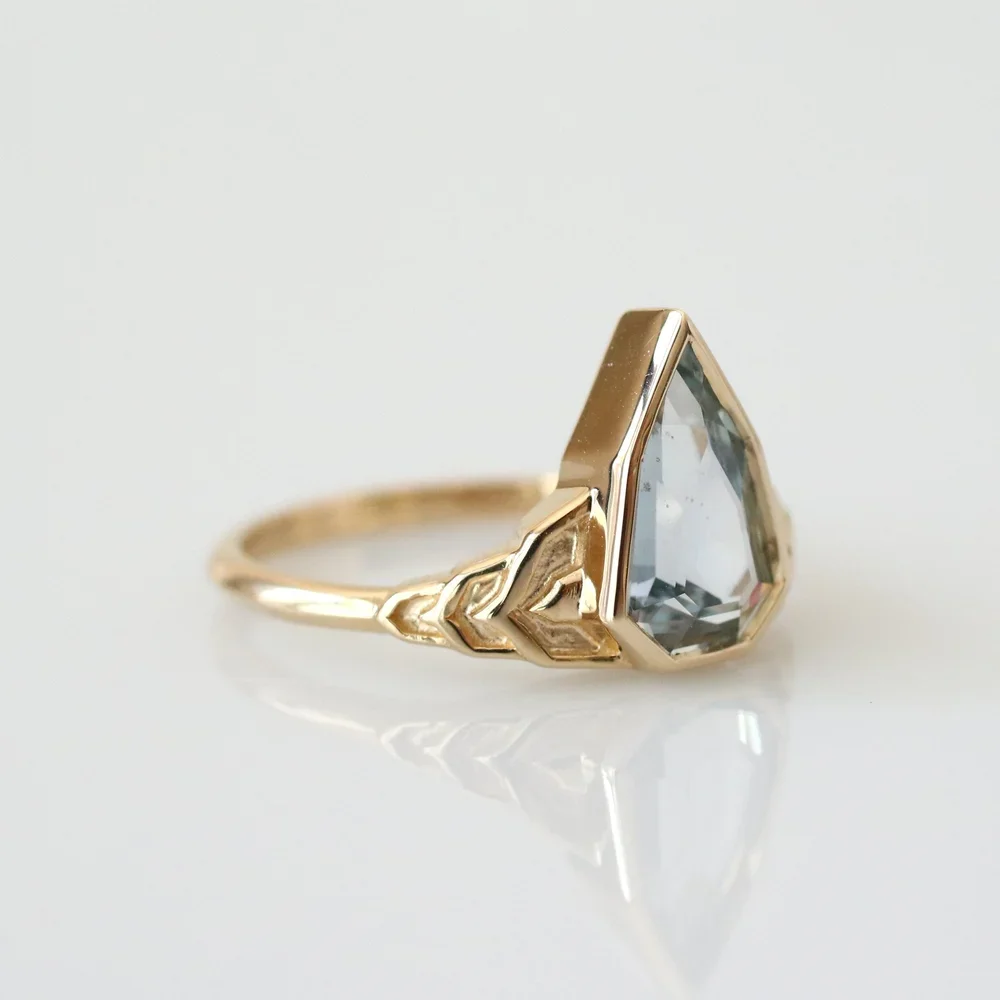 Gold ring with a large, clear gemstone in a geometric setting.