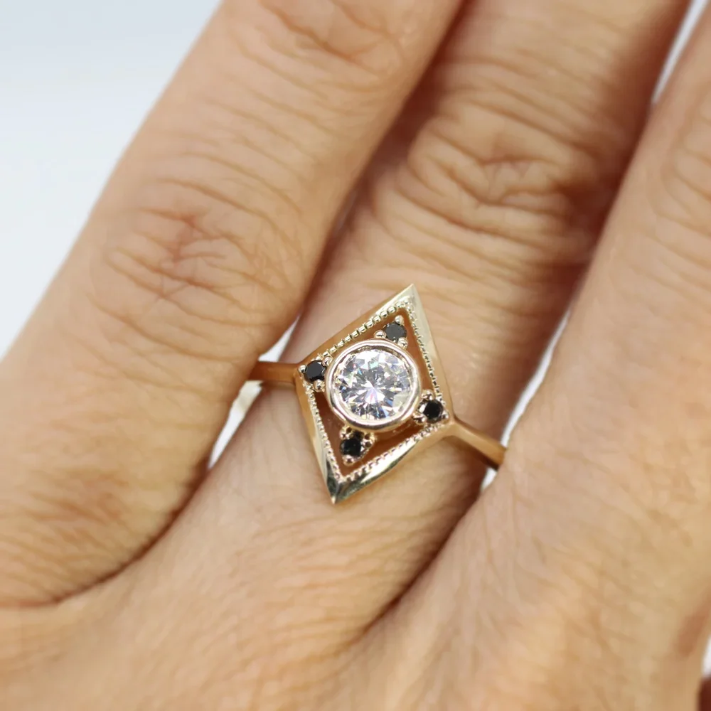 A gold ring with a large central diamond surrounded by small black gemstones in a geometric setting on a person's finger.