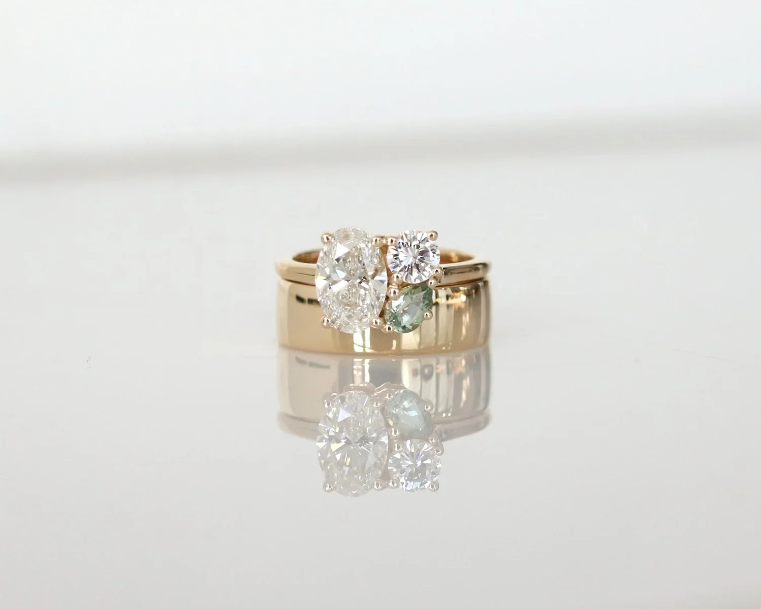 Close-up of three gold rings with large diamonds, placed on a reflective surface with a blurred, light background.