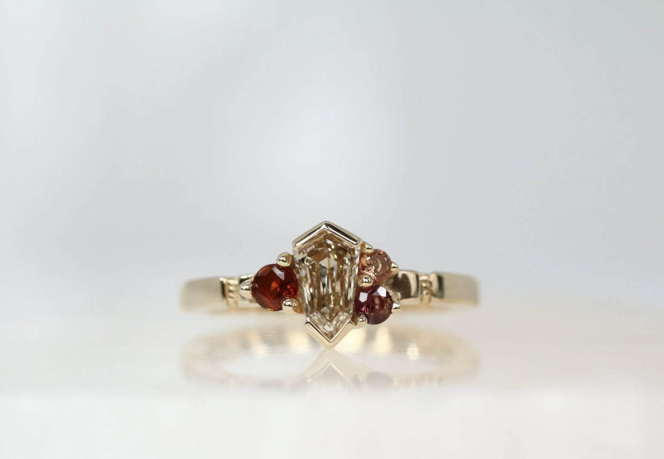 Close-up of a ring featuring a central rectangular clear gemstone, flanked by small heart-shaped red gemstones on each side, set in a gold band.