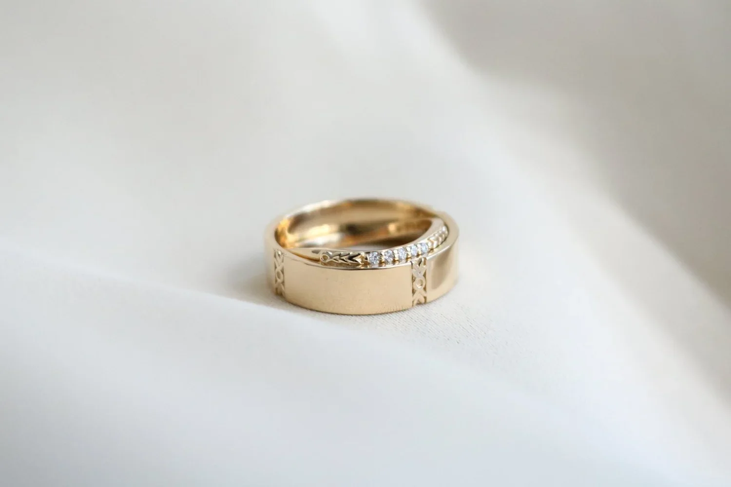 A gold ring with embedded small diamonds rests on a soft white surface.