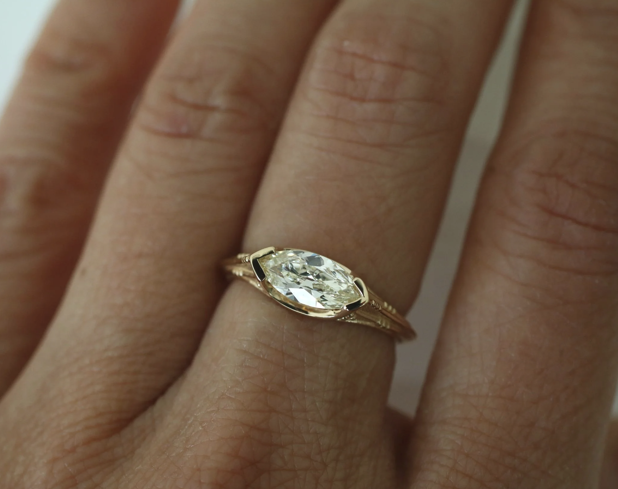 Close-up of a hand wearing a gold ring with a large marquise-cut diamond setting.