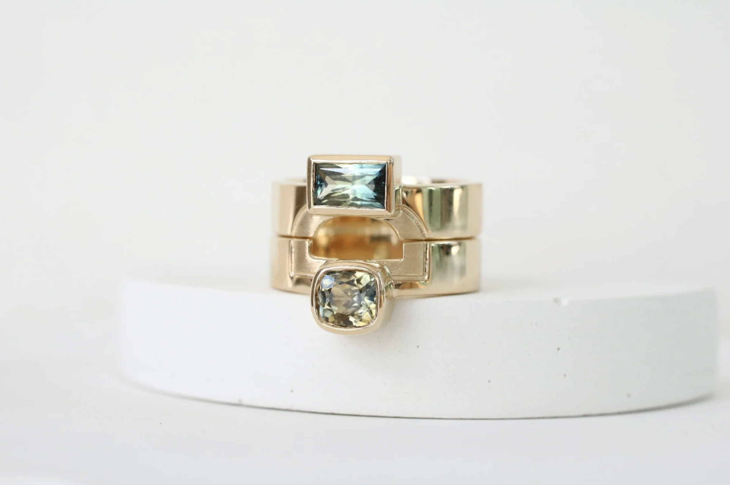 Stack of three gold rings with rectangular and cushion-cut gemstones on white platform