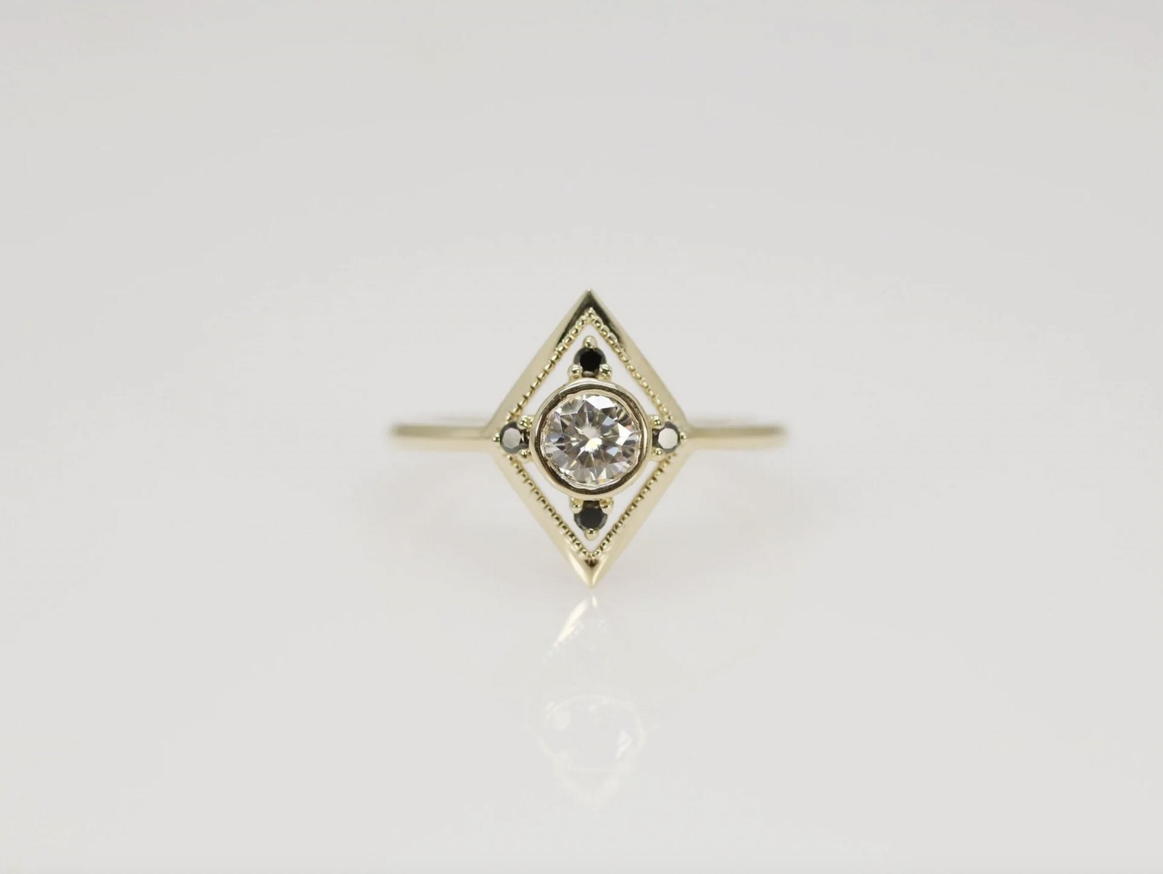 A gold ring with a central round diamond, set within a diamond-shaped frame with small black and white accents.