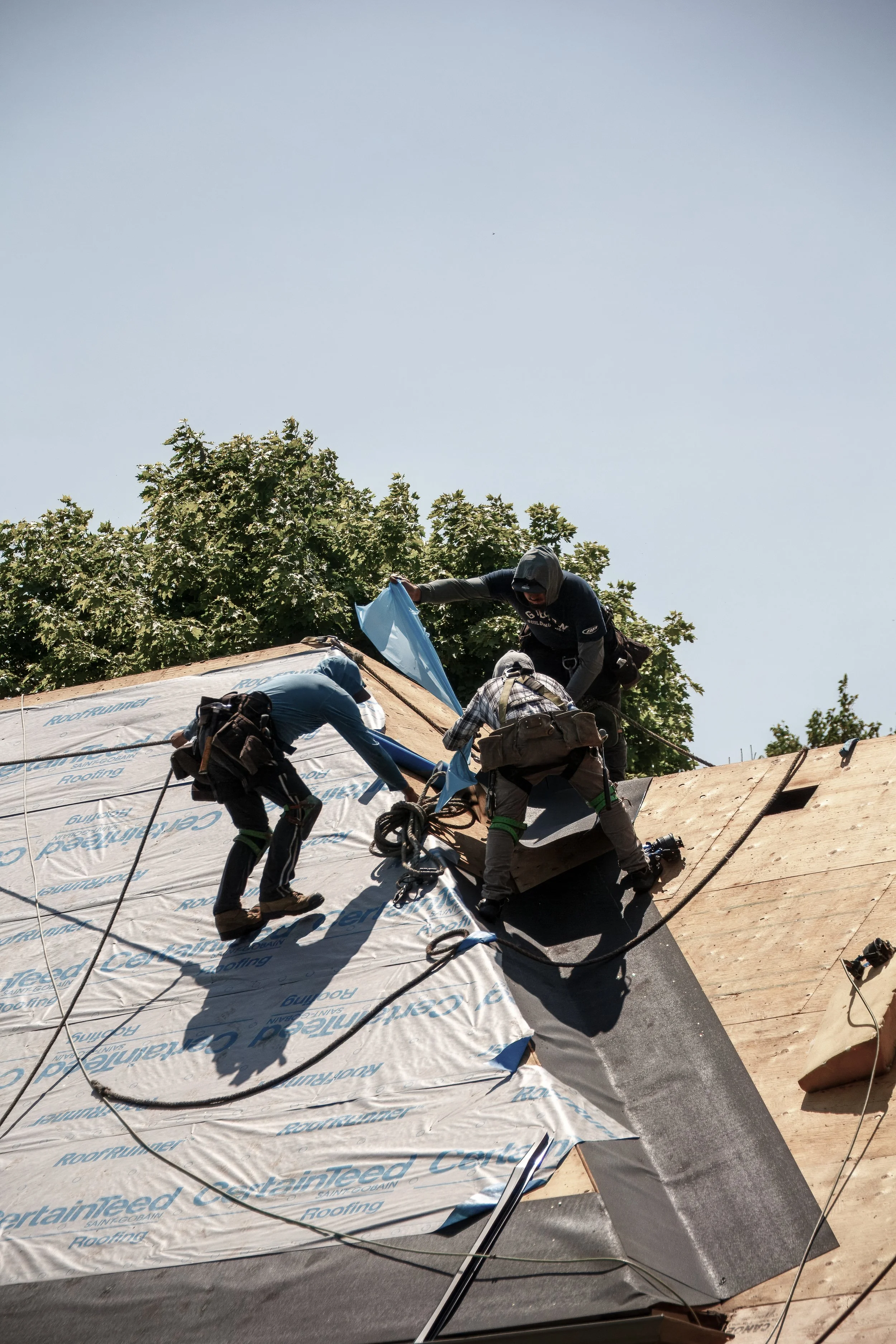 Three roofers working together on a steep roof, installing new roofing material.