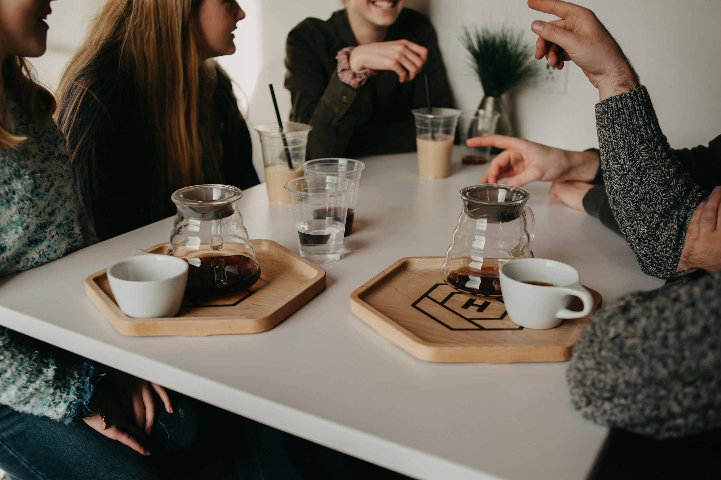 Group of people sitting around a table with coffee and tea, engaged in conversation, with glasses of water, coffee pots, and cups on trays.