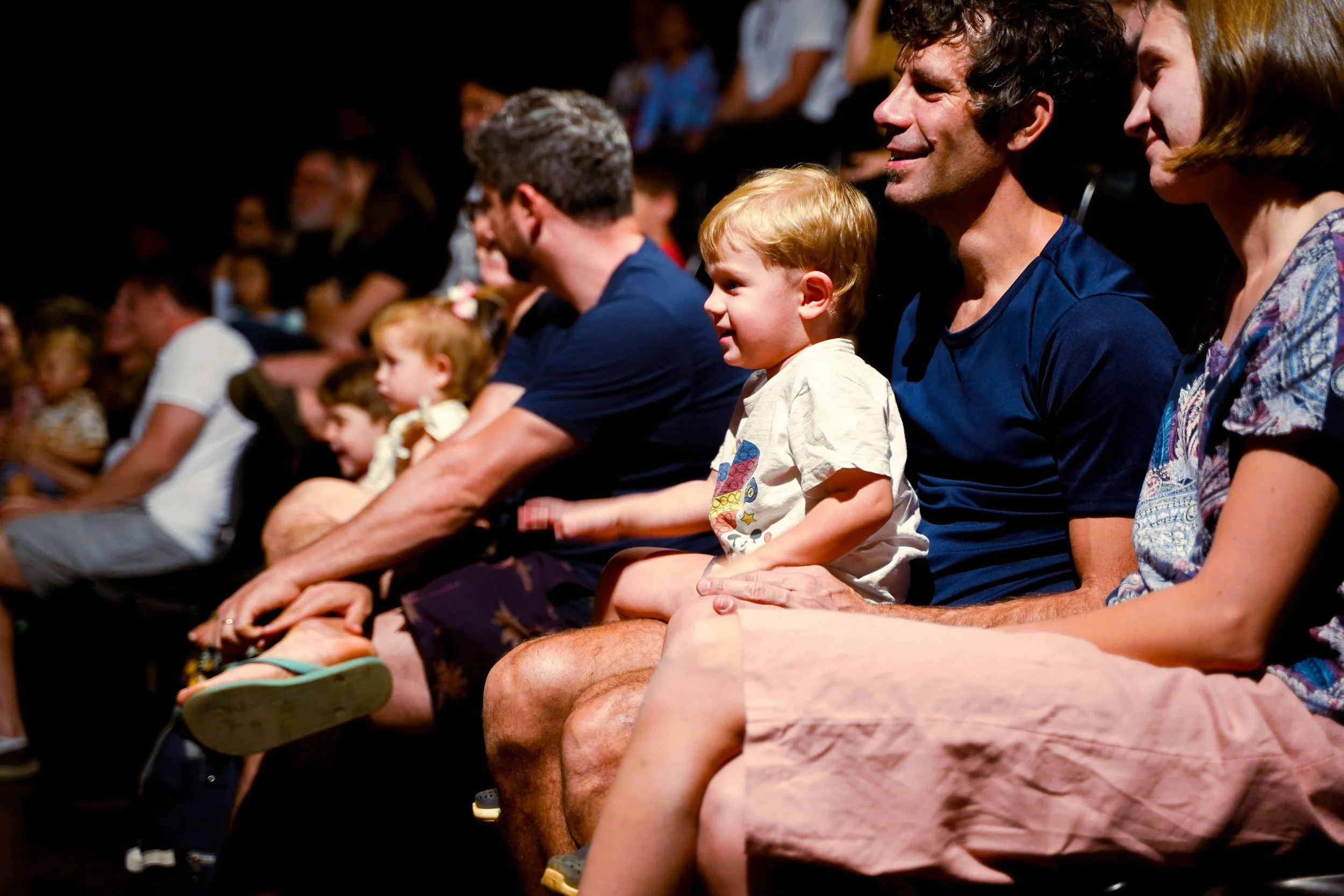 Family and children sitting in an audience attending a show or performance, with some adults and children smiling and focused on the stage. Curated Event Listings in Columbia, Maryland