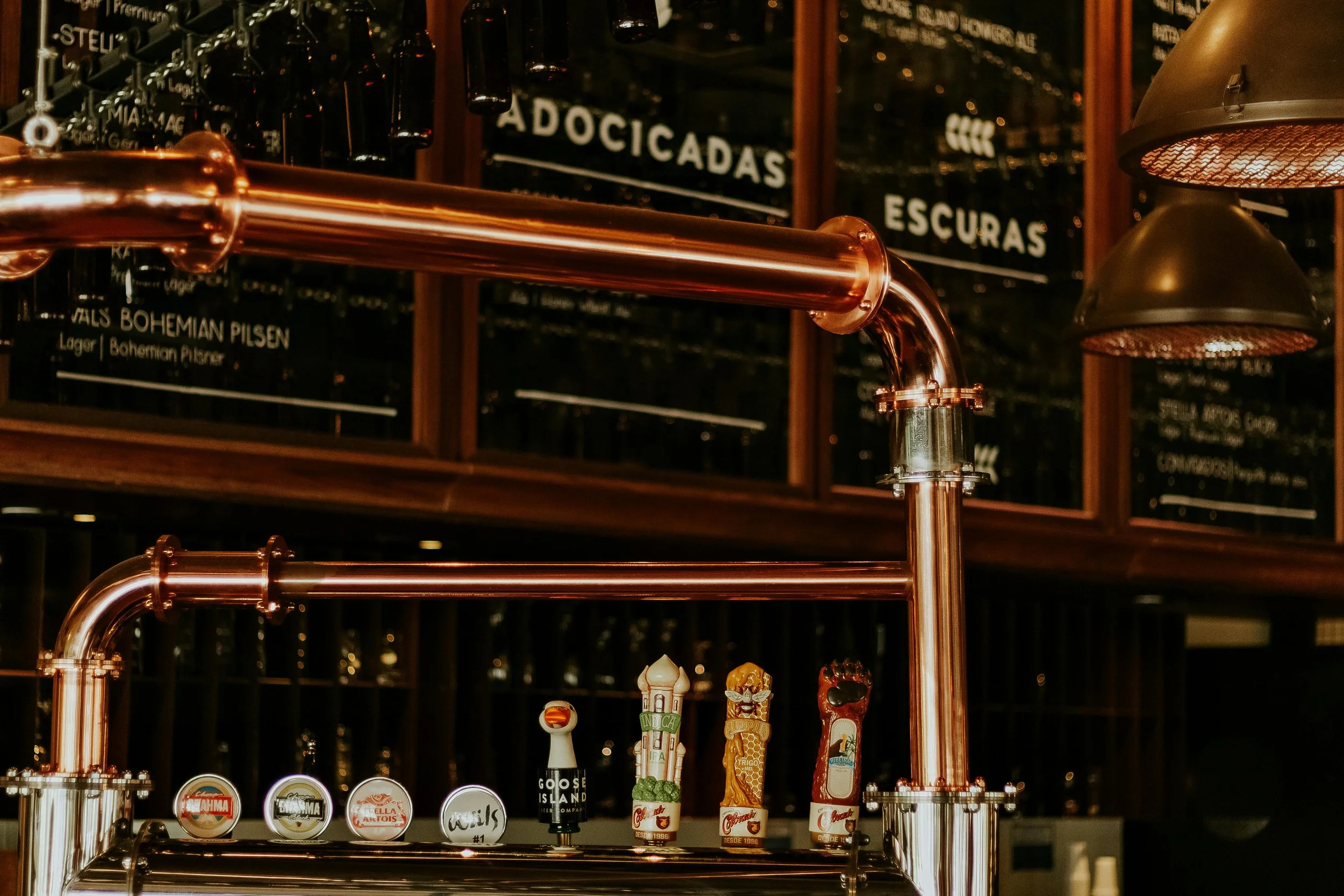 Copper pipes forming part of a bar draft system with beer tap handles and a menu board in the background. Curated Event Listings in Columbia, Maryland