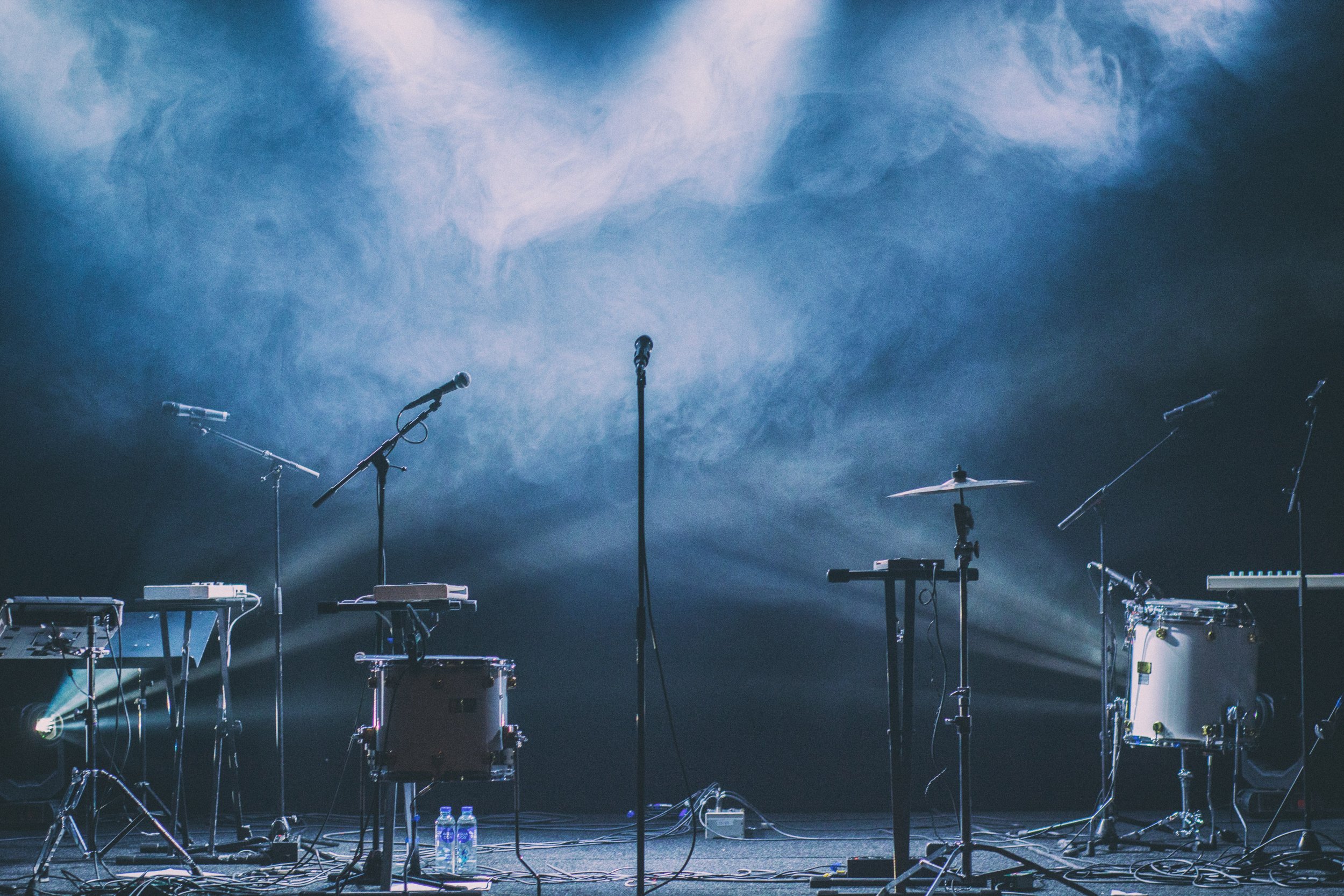 Empty stage with musical instruments including drums, keyboards, microphones, and stands, with stage lighting and smoke effects. Curated Event Listings in Columbia, Maryland