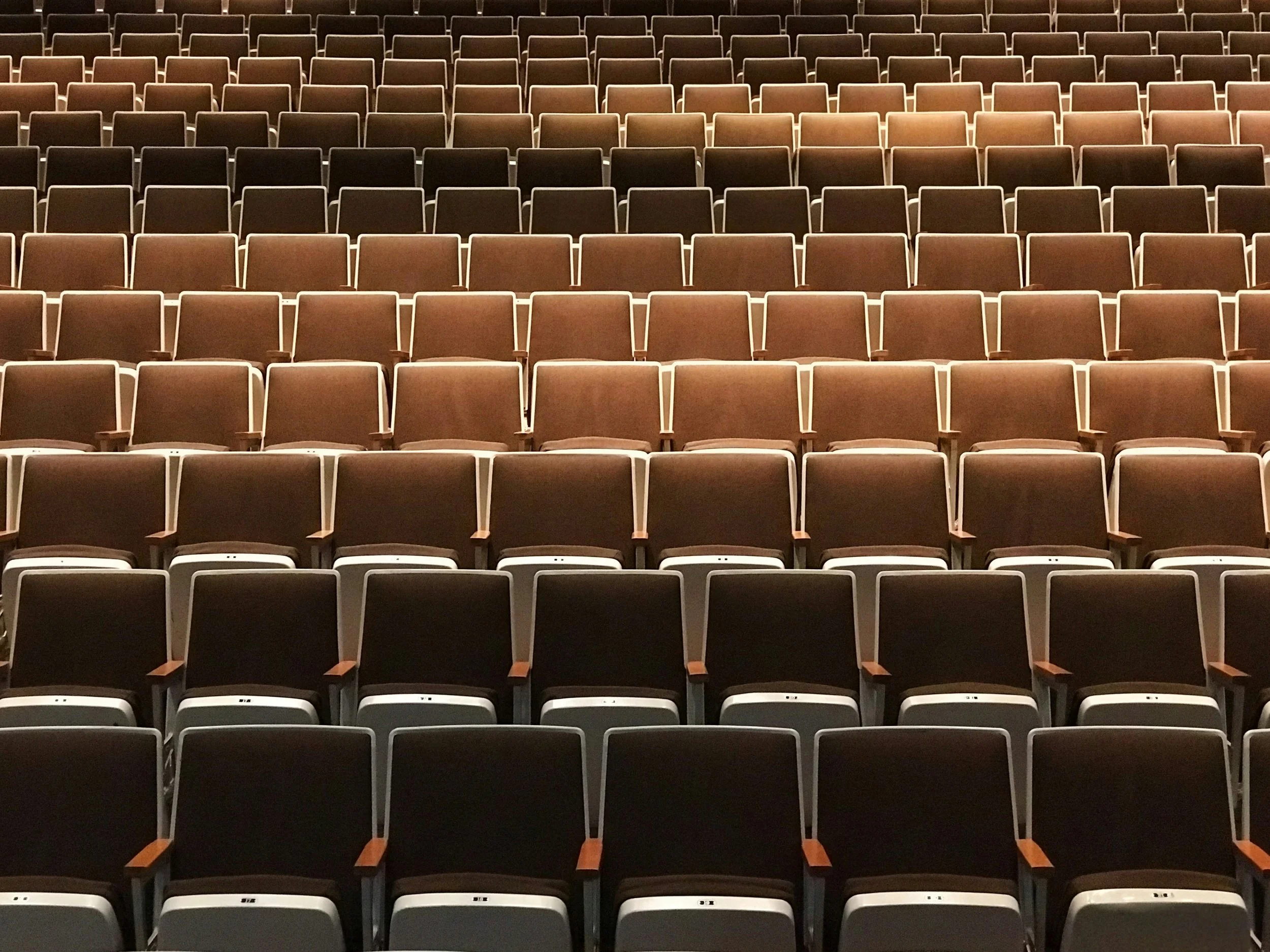 Empty auditorium with rows of brown and black chairs.