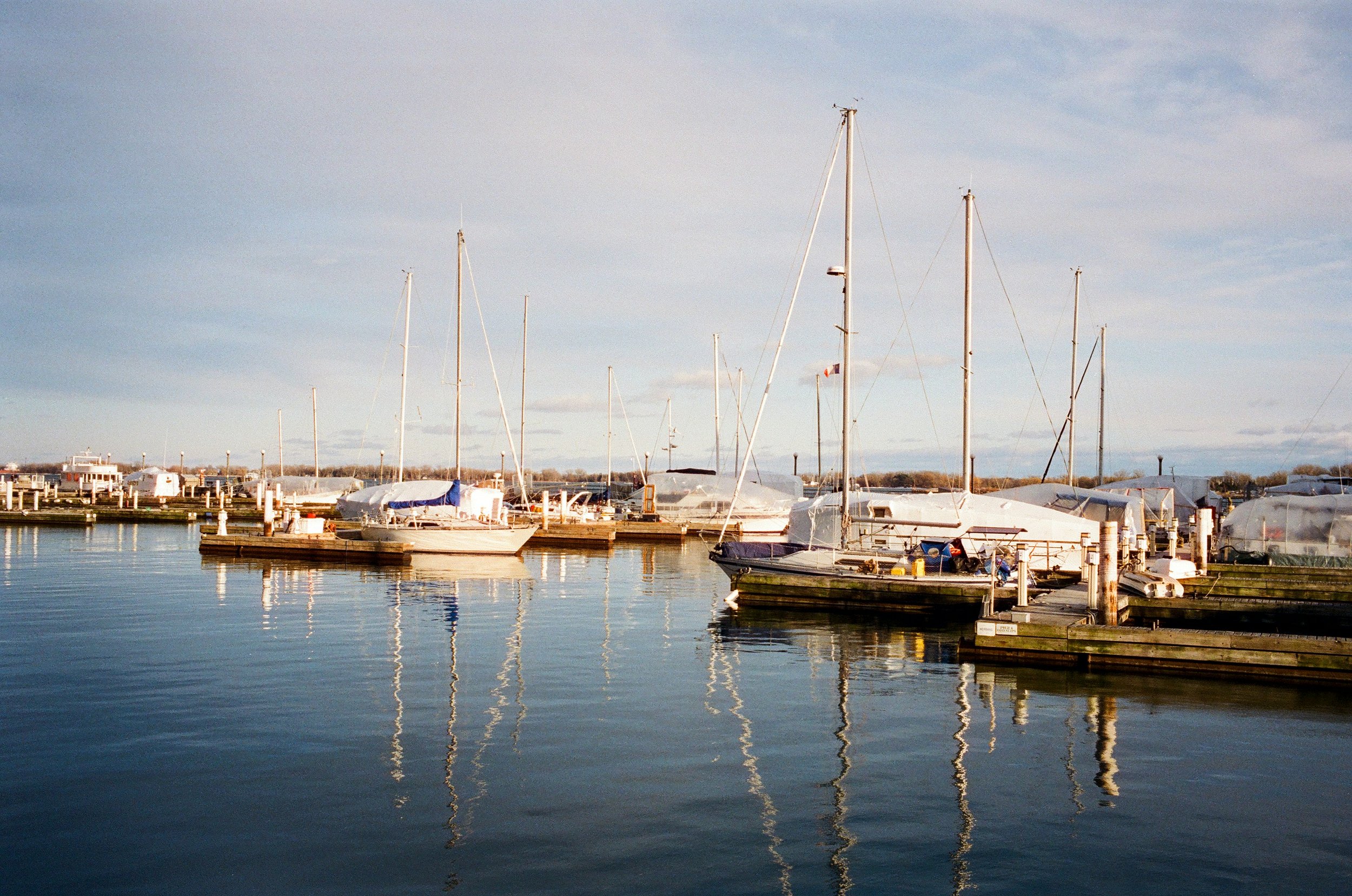 Sailboats docked at a marina with calm water and a cloudy sky.