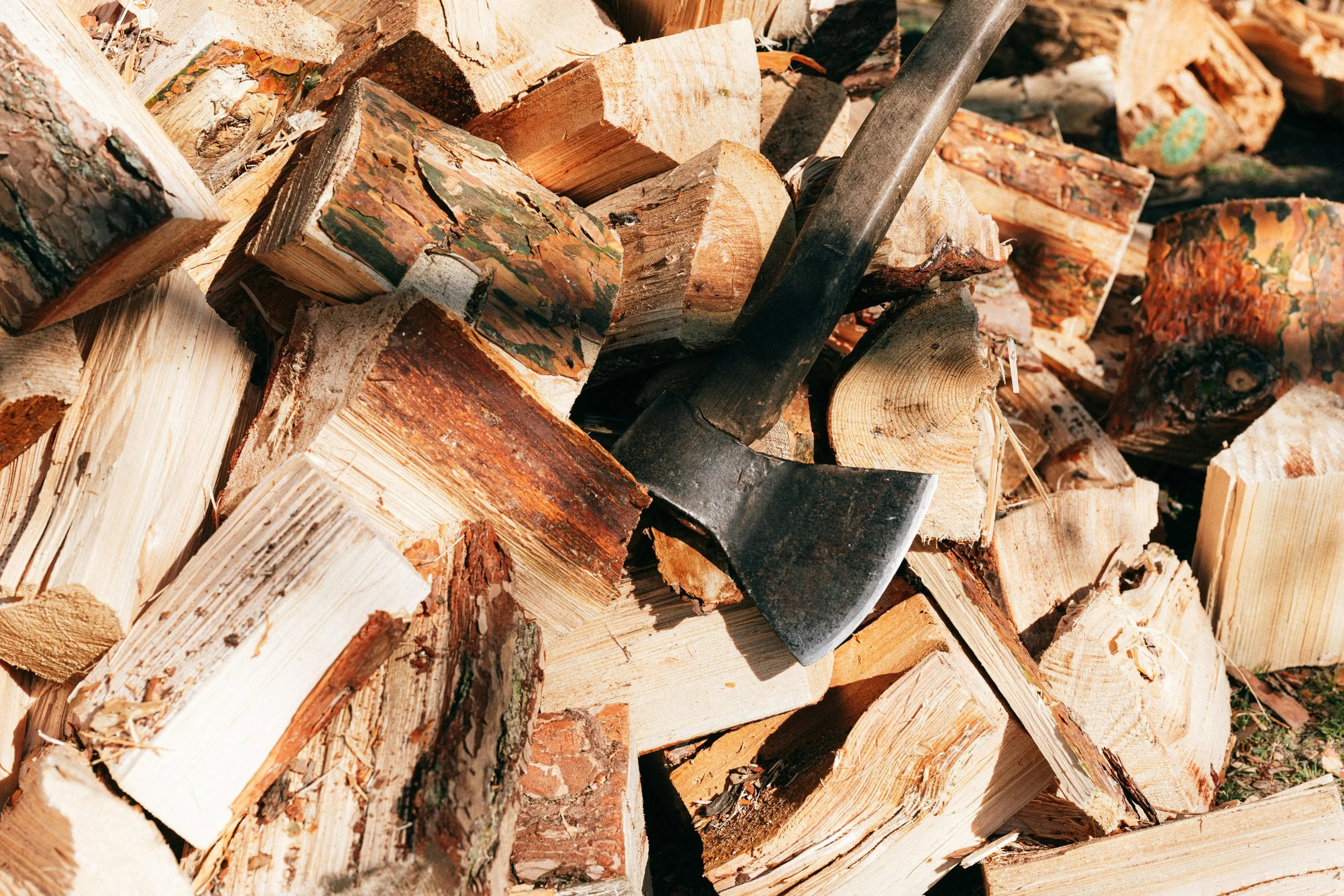 A pile of chopped firewood with an axe embedded in some logs.