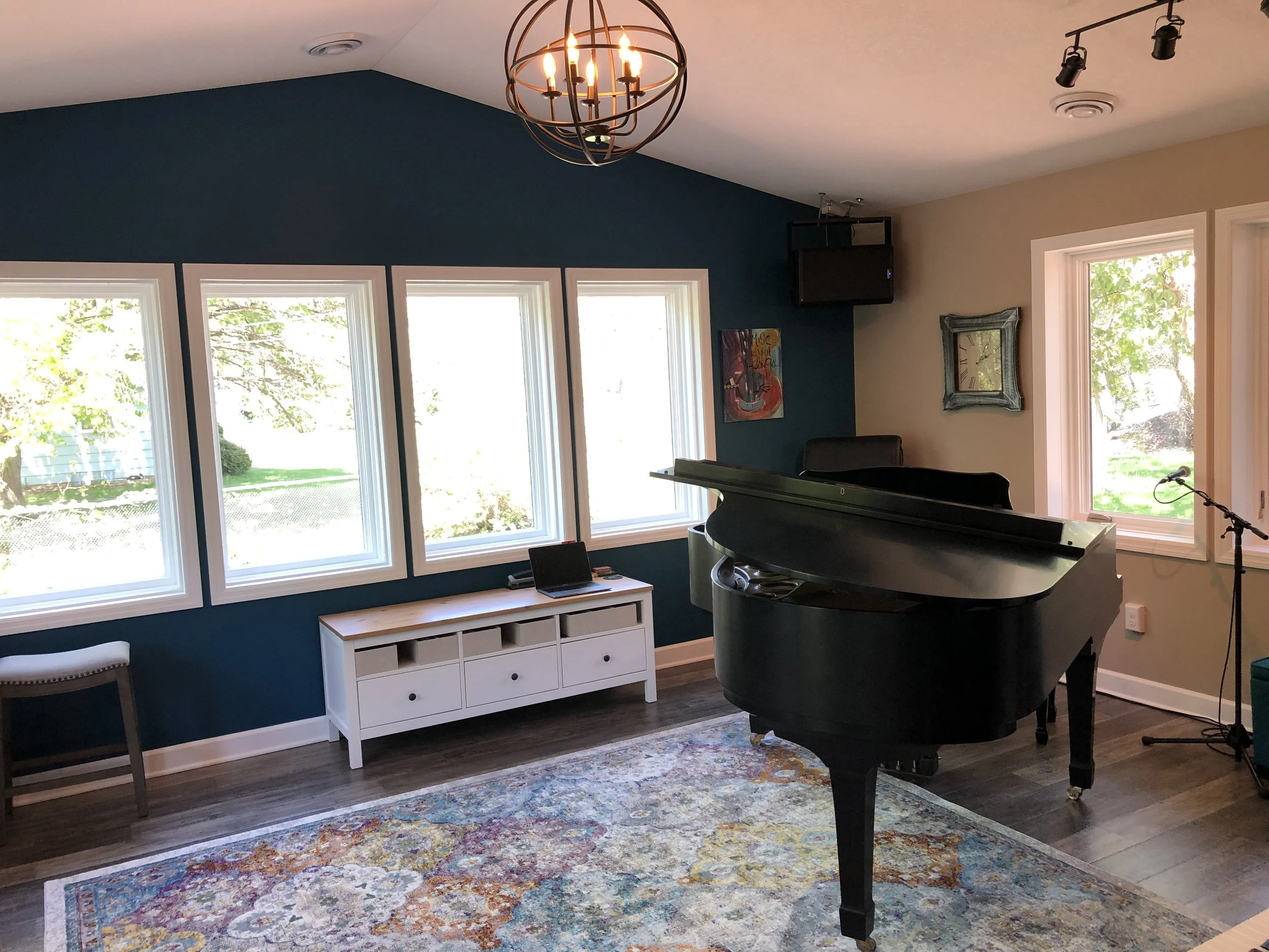 Interior of a music room with a black grand piano, large windows, a colorful area rug, and a blue accent wall. Music studio located in Lake Elmo, MN serving Stillwater, Woodbury and Mahtomedi.