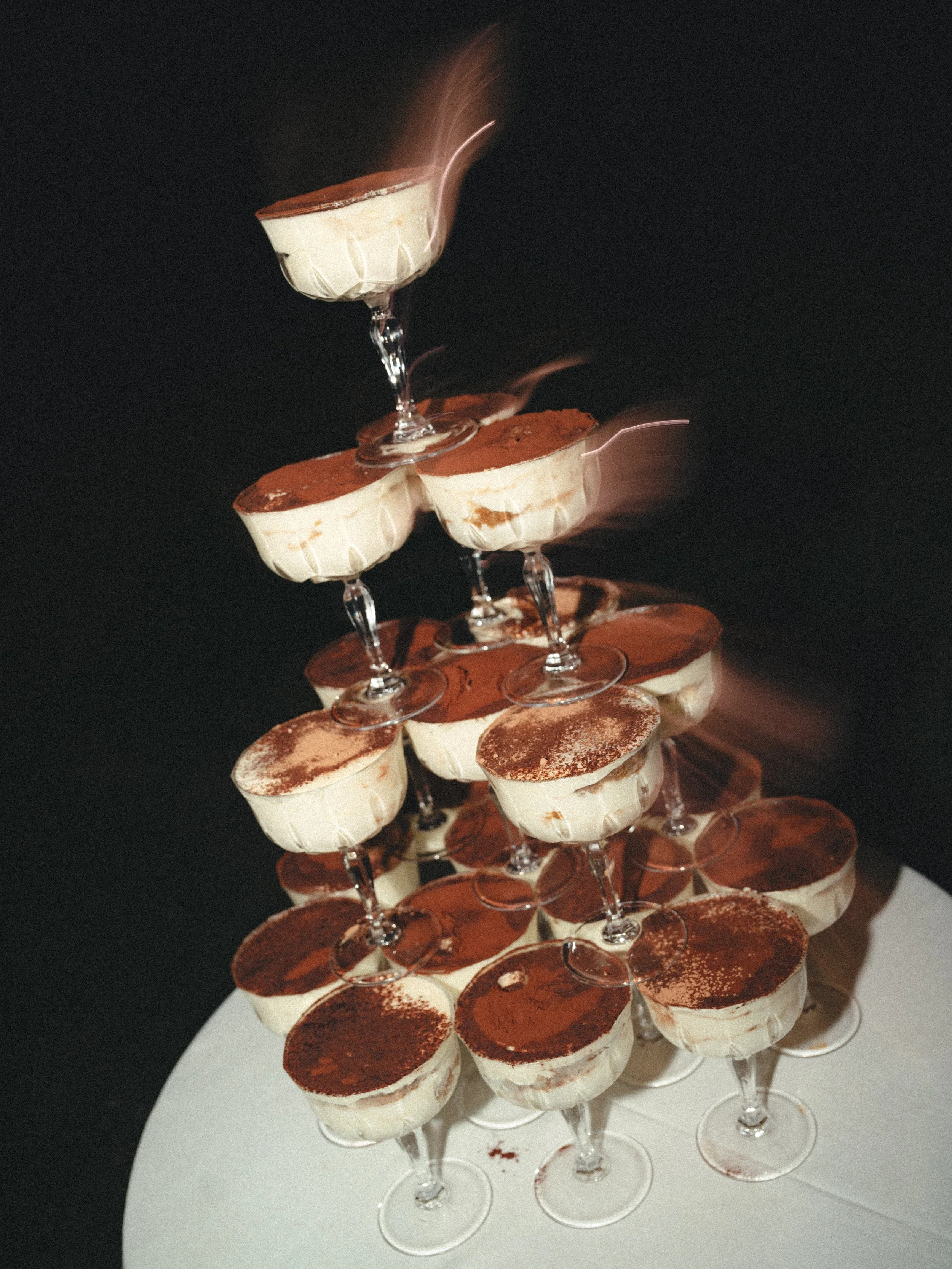 Tiramisu desserts arranged in a pyramid shape in wine glasses with cocoa powder on top, against a dark background. Luxury planning and experiences. Dessert. Italy.