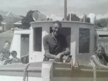 Man standing on a boat with several children seated nearby, in a black-and-white photo.