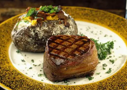 A grilled steak and a loaded baked potato on a decorative plate with green garnish.