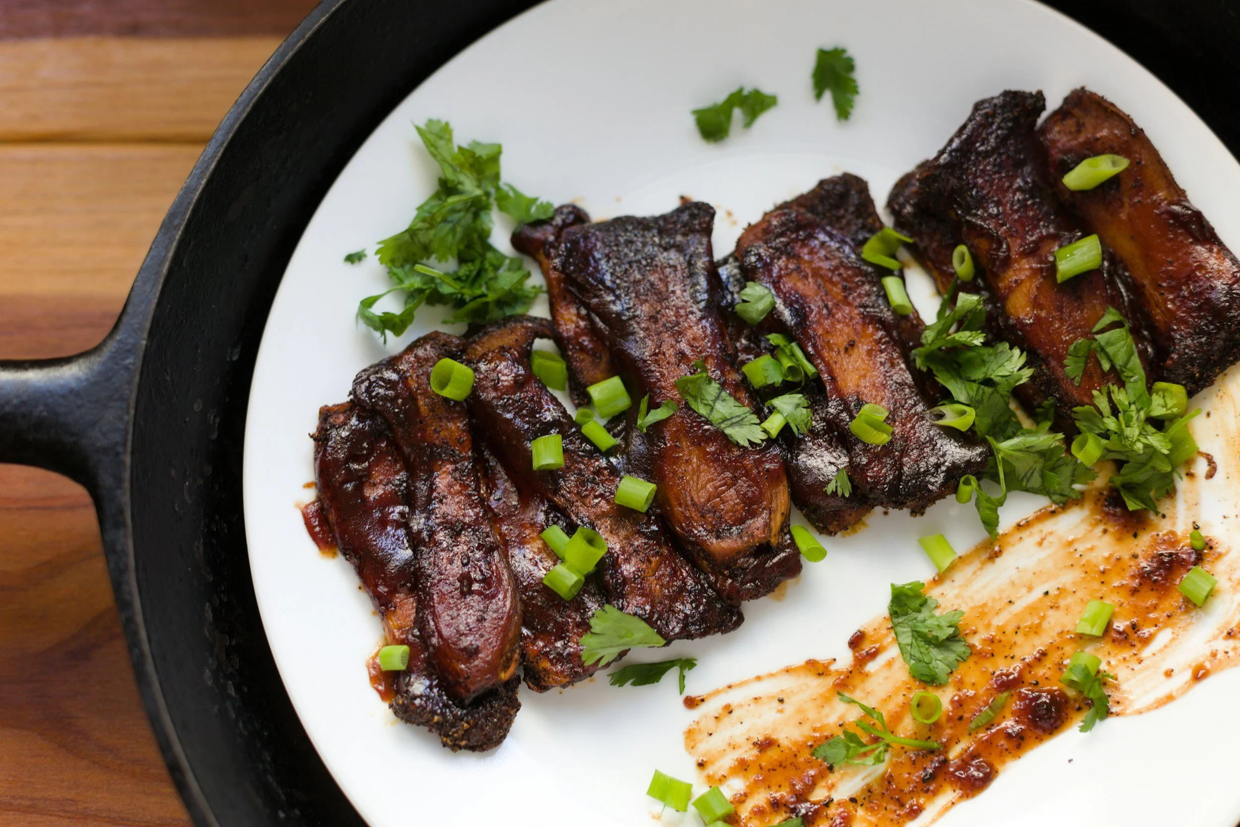 Barbecued pork ribs garnished with chopped green onions and cilantro on a white plate, with a smear of barbecue sauce.
