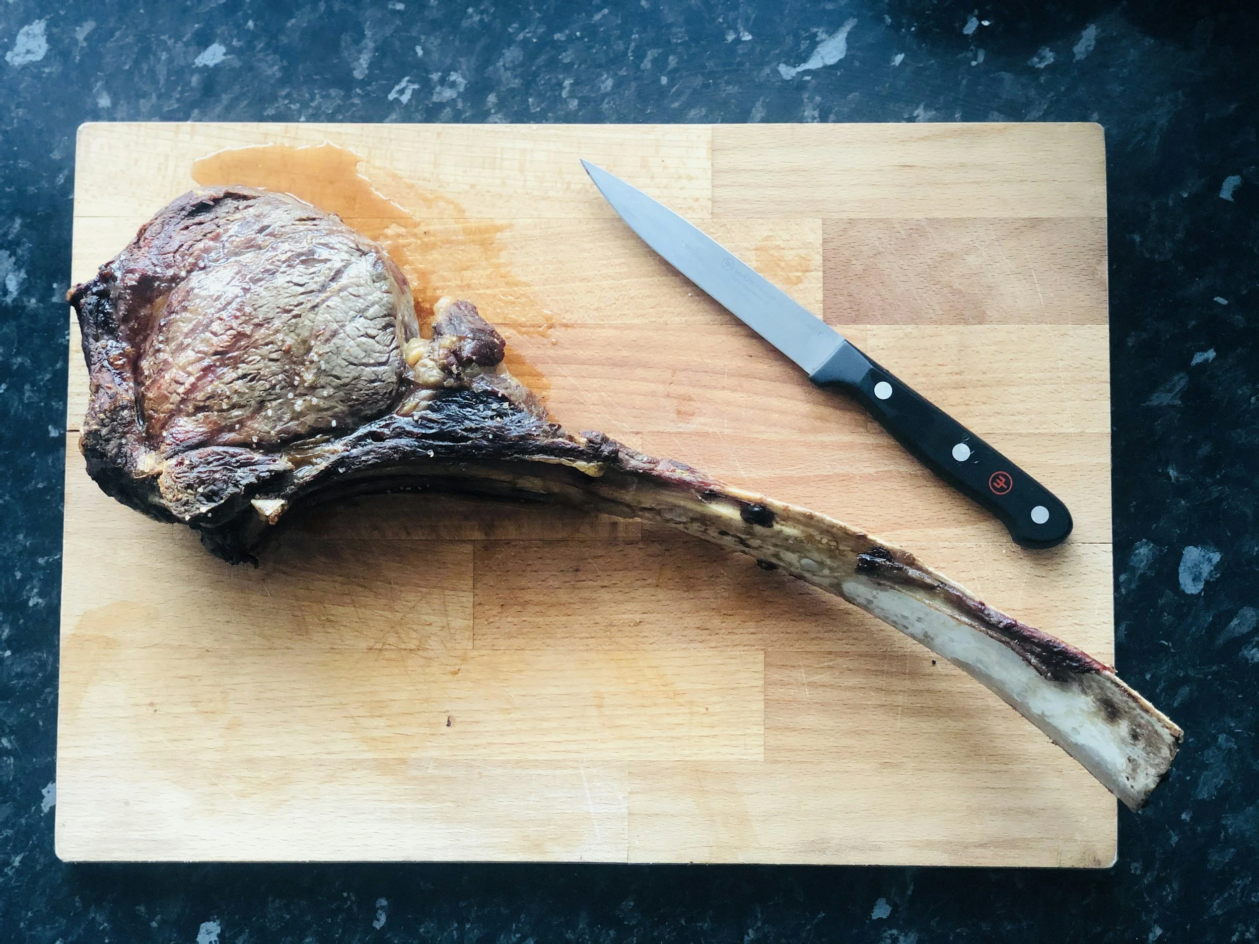 A cooked bone-in steak on a wooden cutting board with a black-handled knife nearby.