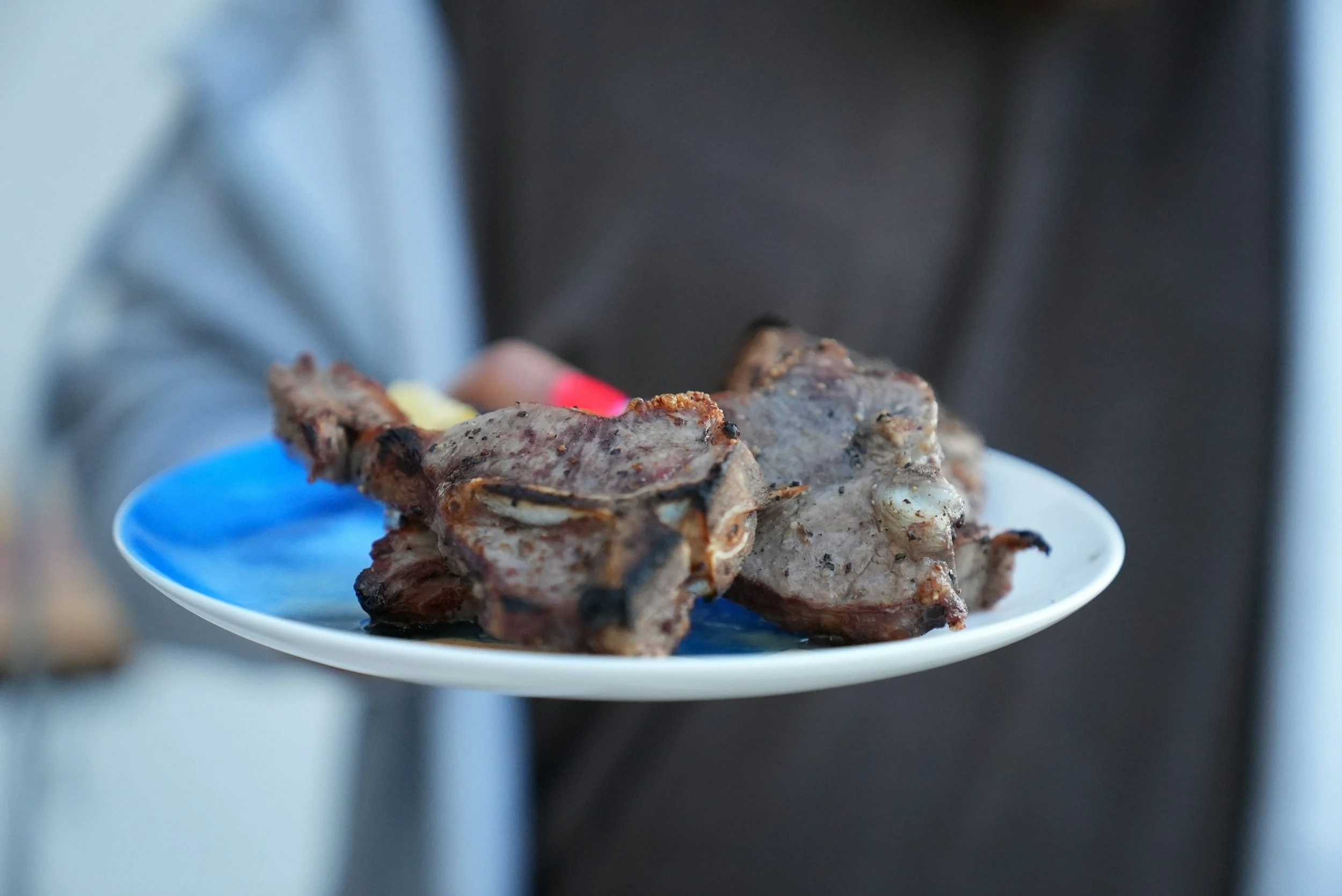 Person holding a white plate with cooked ribs.