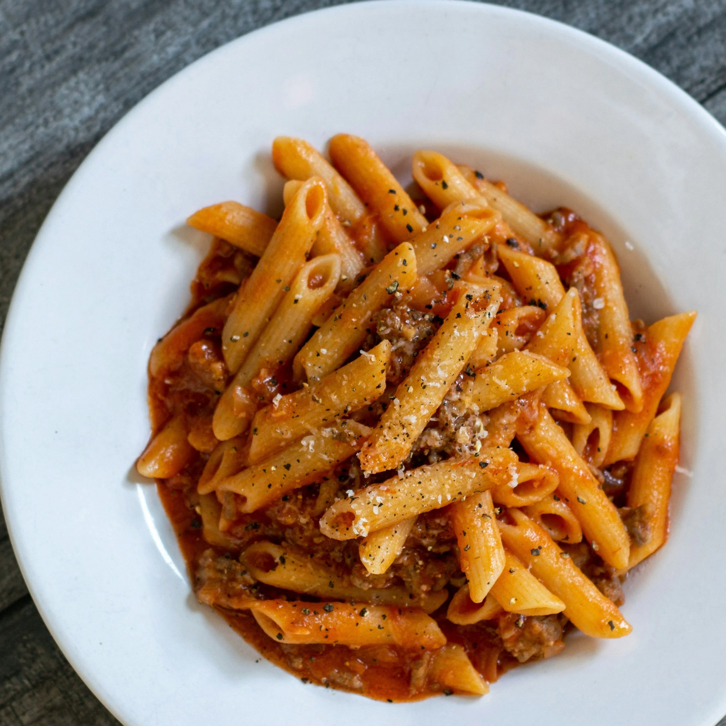 Plate of cooked penne pasta with meat sauce, garnished with black pepper.