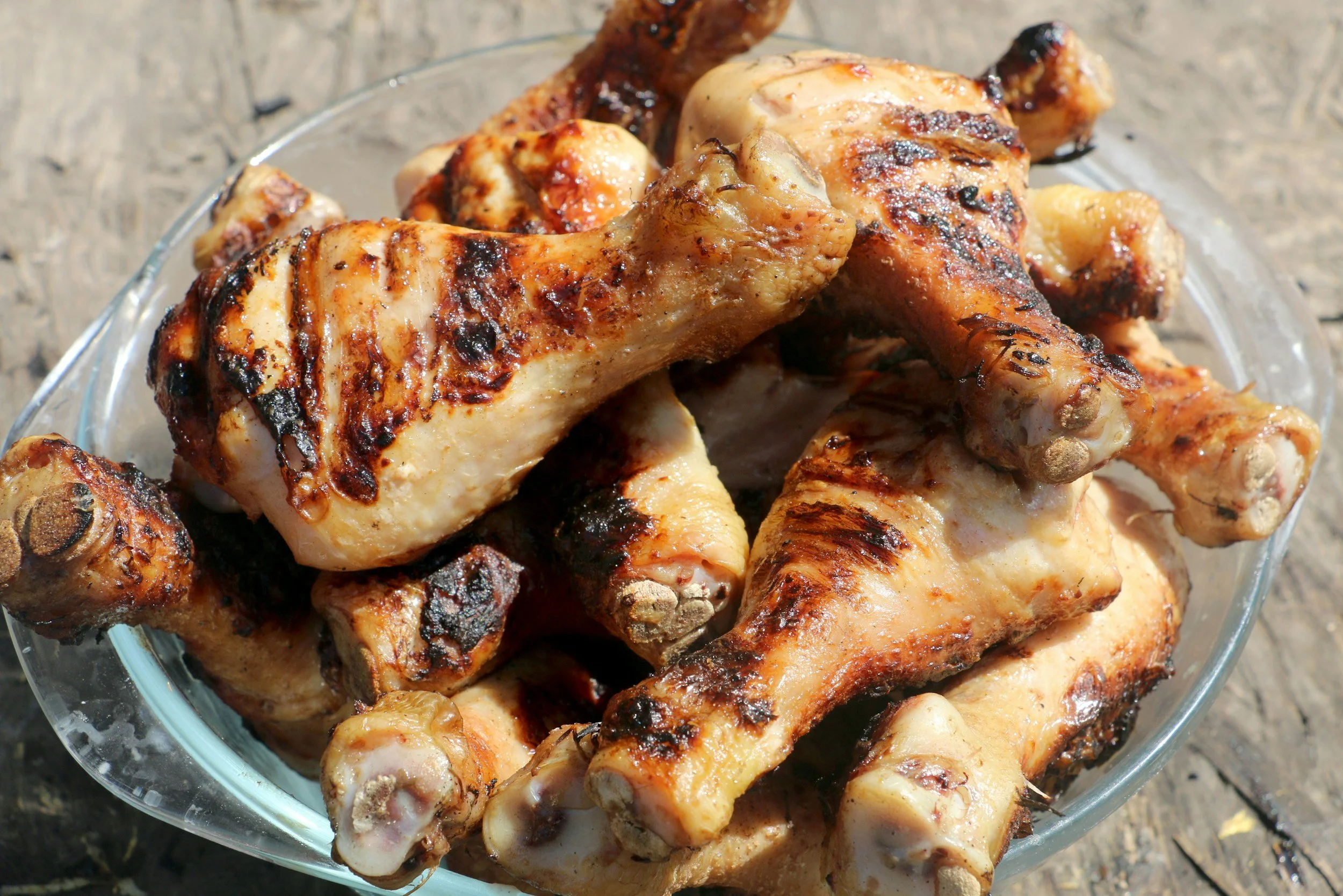 Grilled chicken drumsticks in a glass dish on a wooden surface.