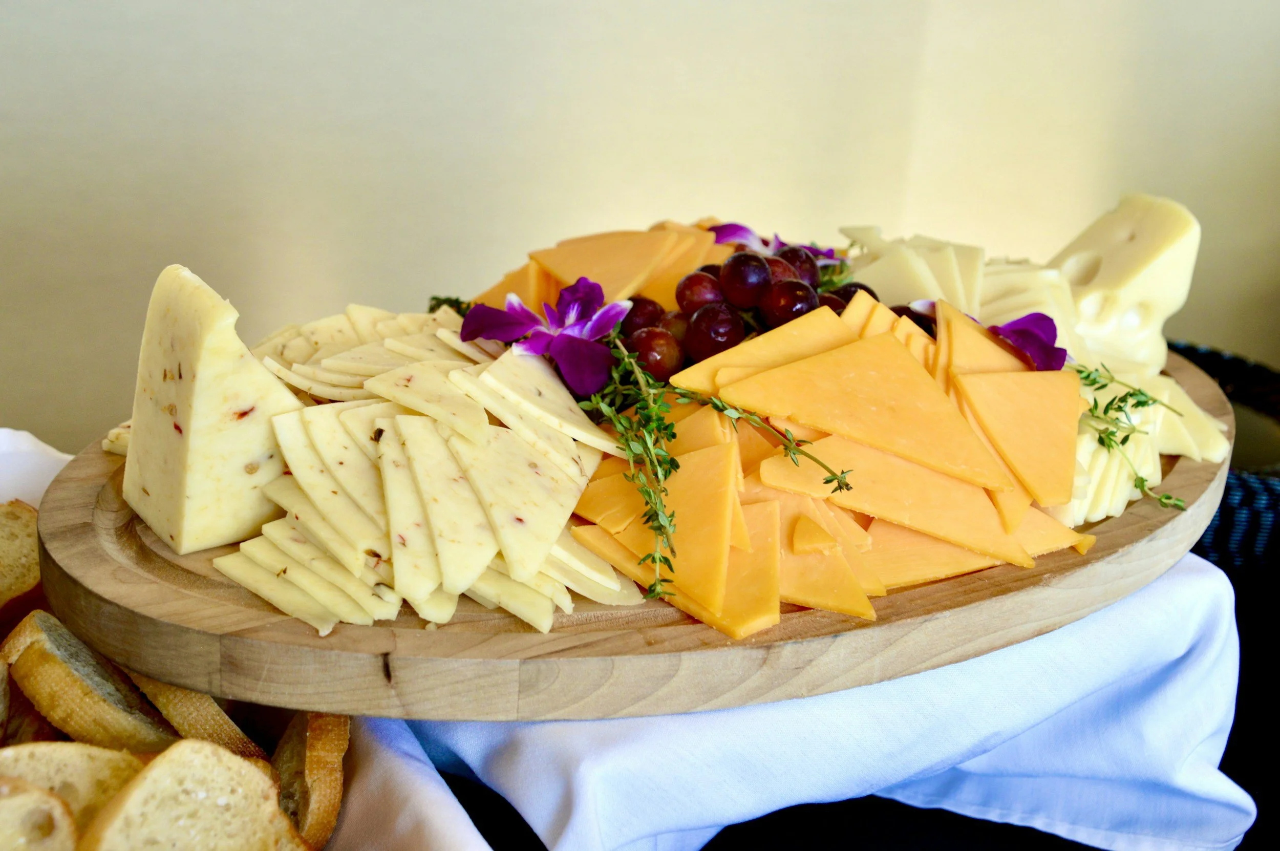 Cheese platter with various cheeses, red grapes, and purple flowers on a wooden board.
