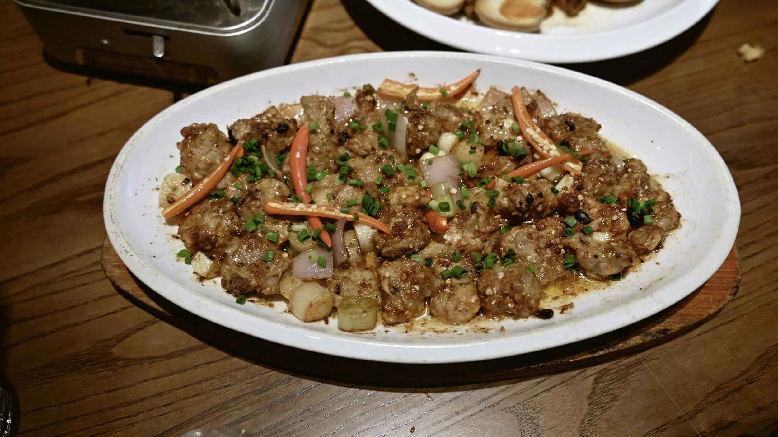 Meatballs with chopped green onions, carrots, and onions on a white dish.