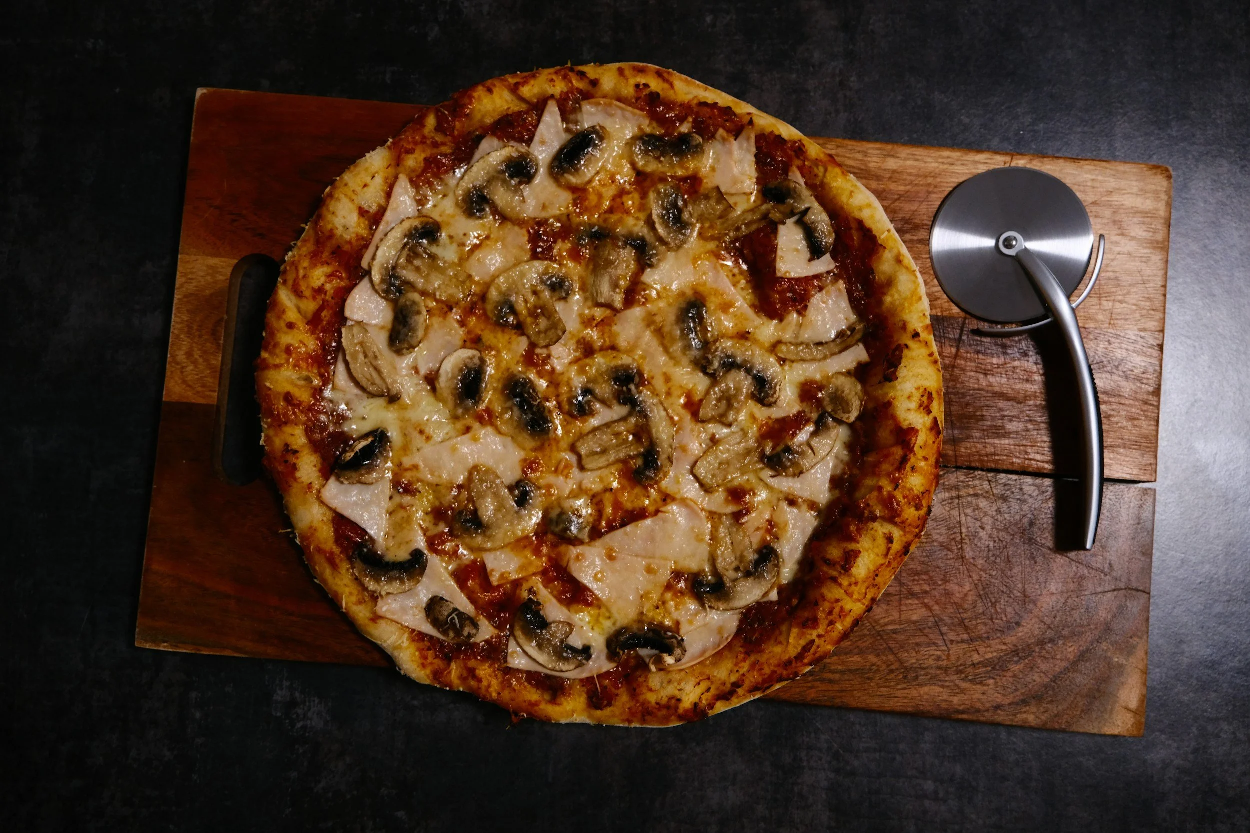 A mushroom and turkey pizza with cheese on a wooden pizza peel.
