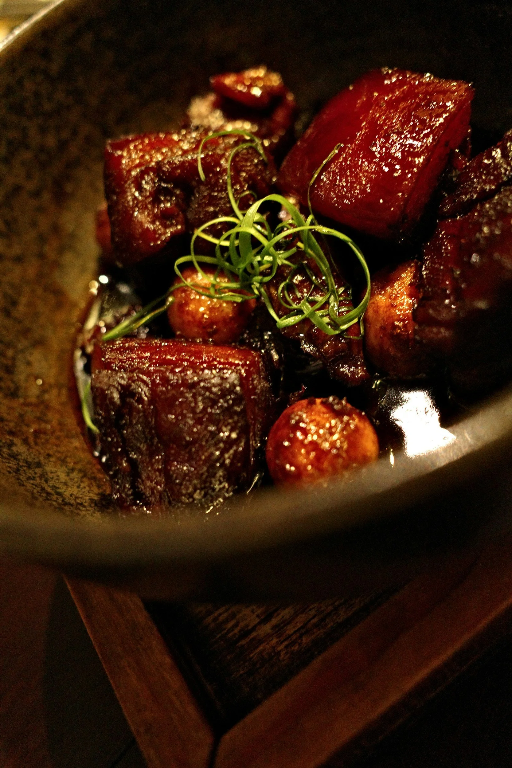 Cooked beef short ribs with a sprig of green garnish, served in a dark bowl.