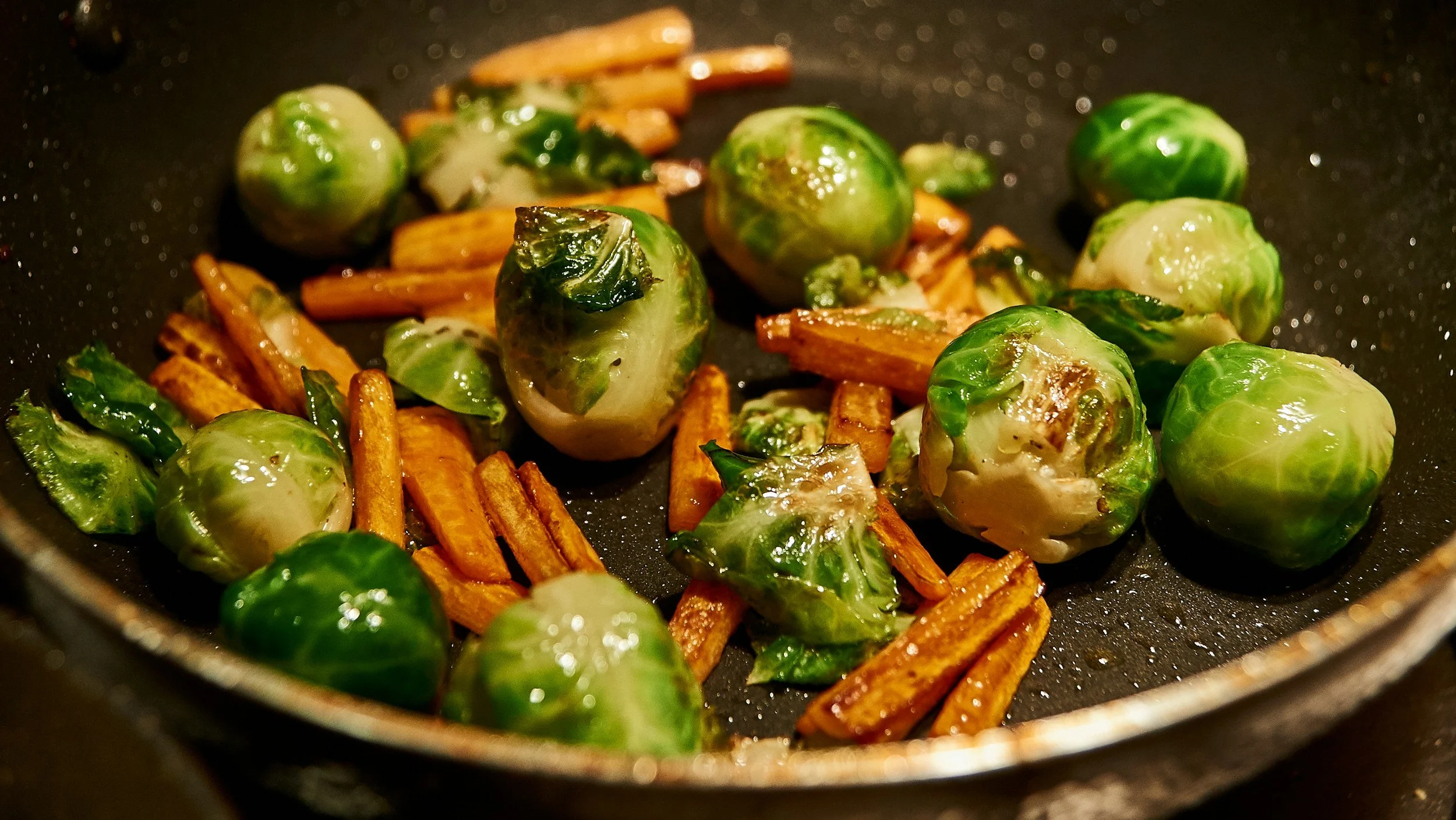 Brussels sprouts and sweet potato fries cooking in a black frying pan.