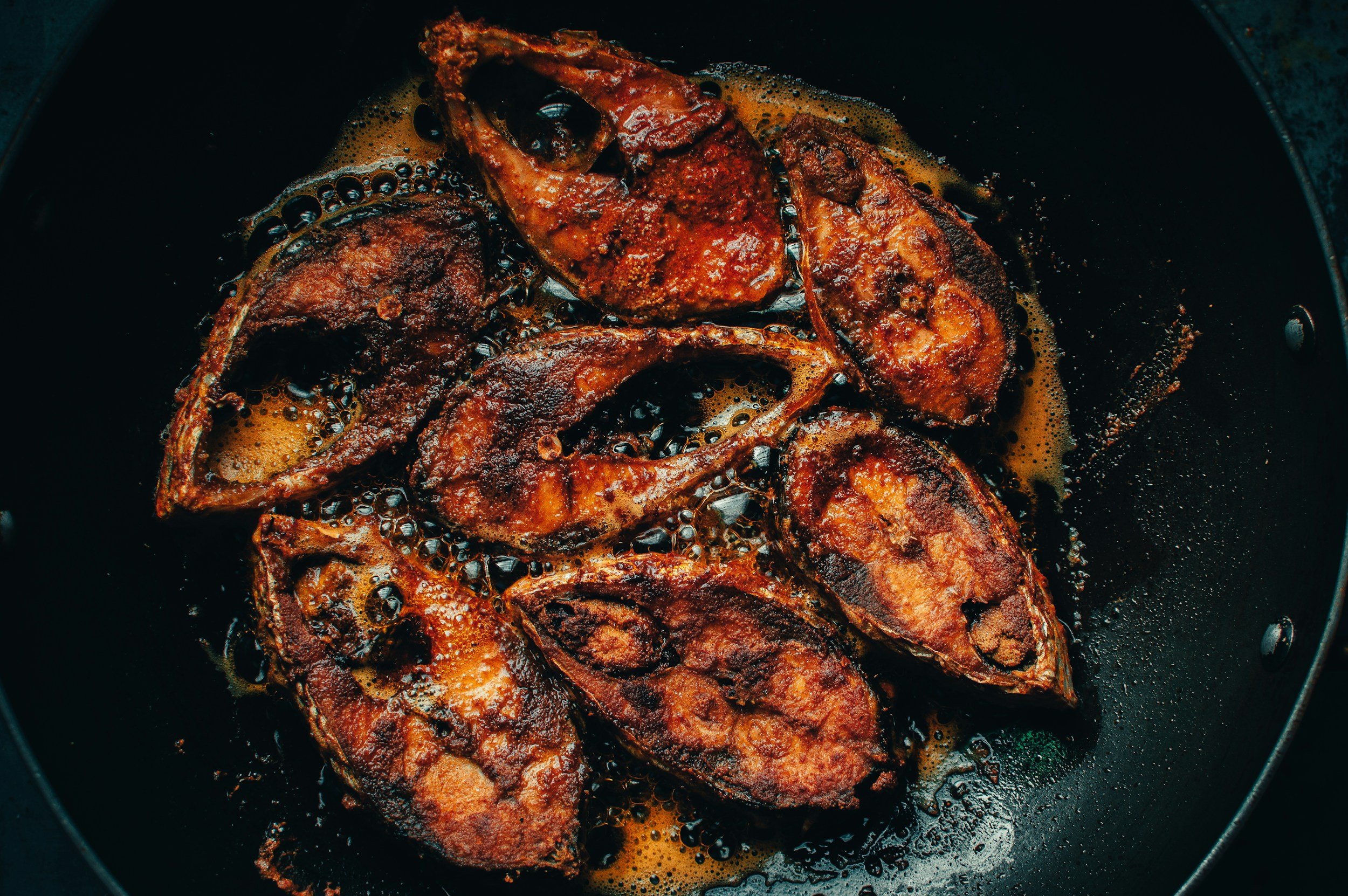 Fried fish pieces cooking in a black skillet with bubbling oil.