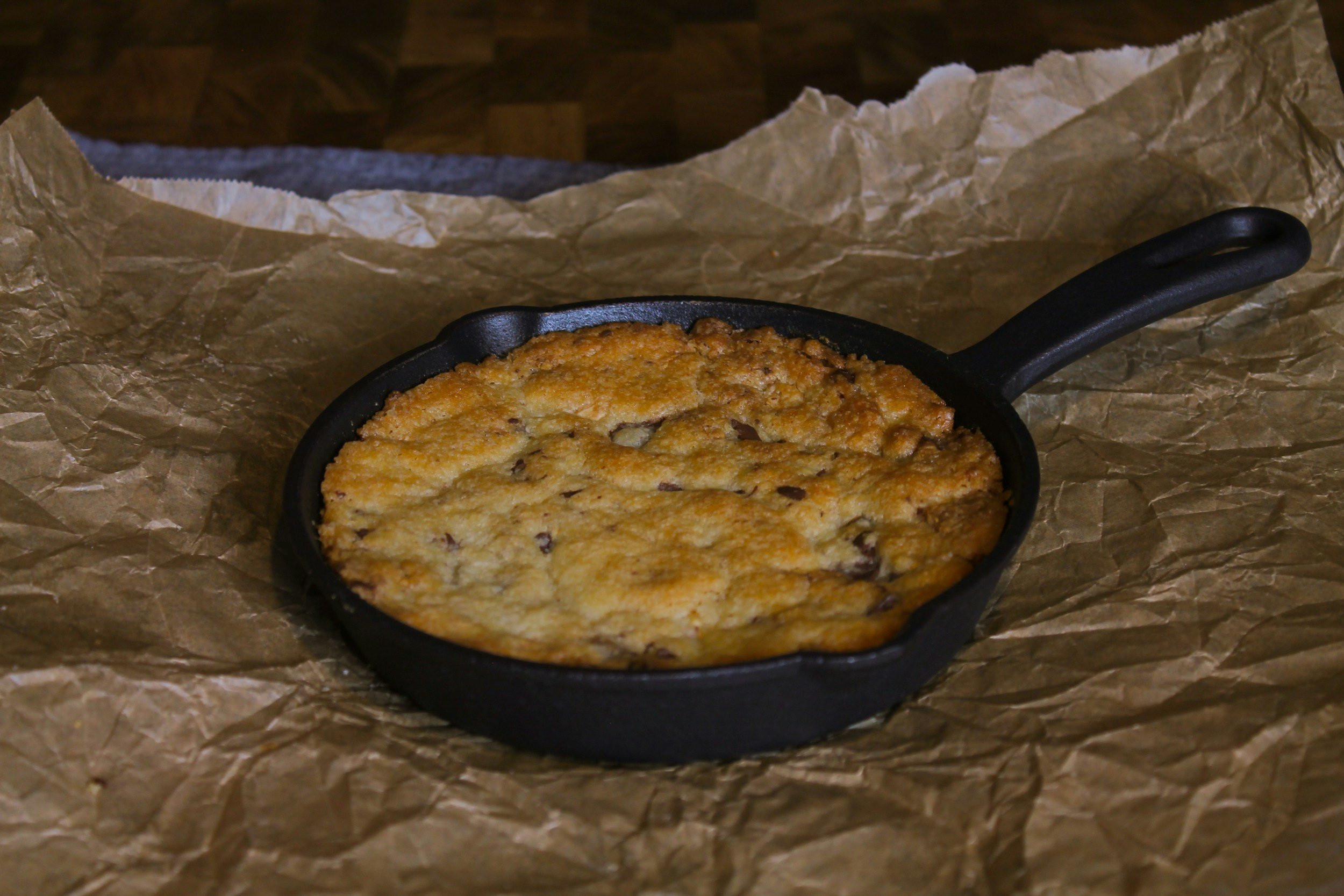 Baked dish in a small black cast iron skillet on crumpled brown parchment paper.