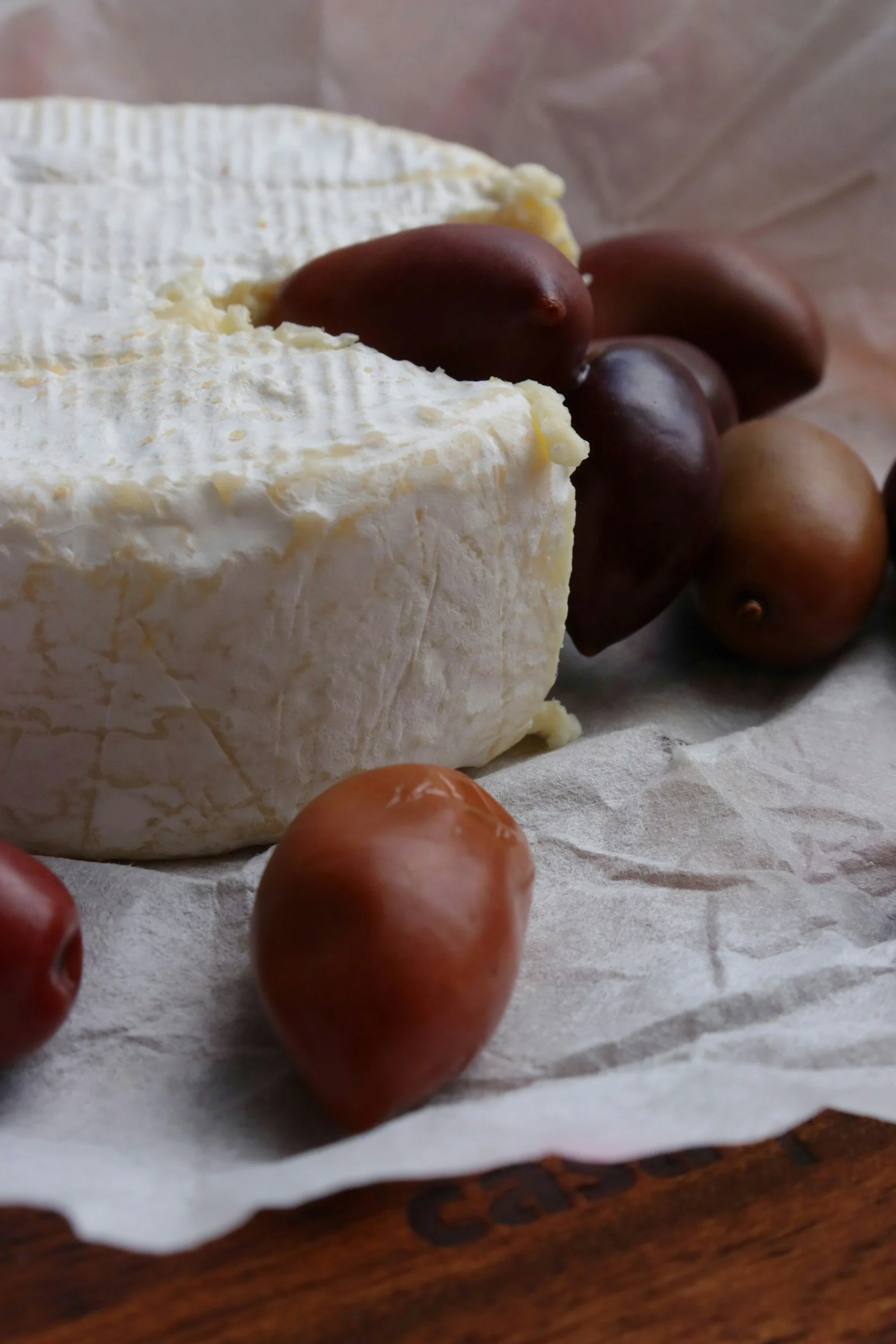 A wedge of soft, creamy Brie cheese accompanied by red, brown, and yellow grapes on parchment paper.