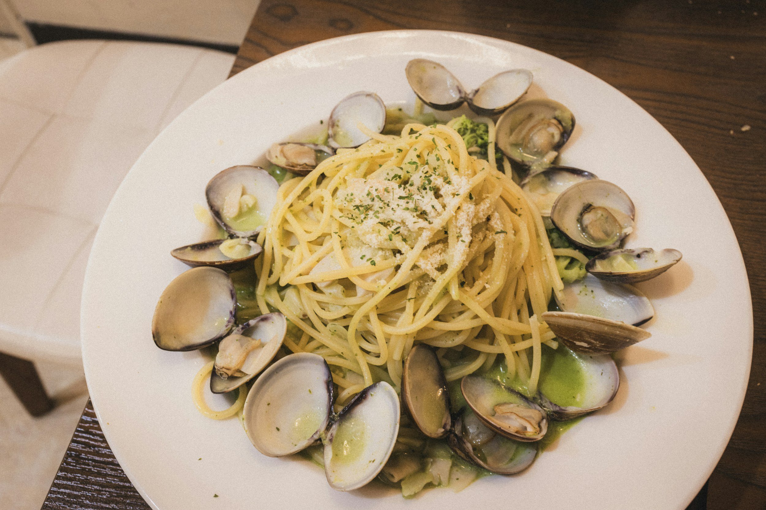 Plate of spaghetti with clams, garnished with grated cheese and herbs.
