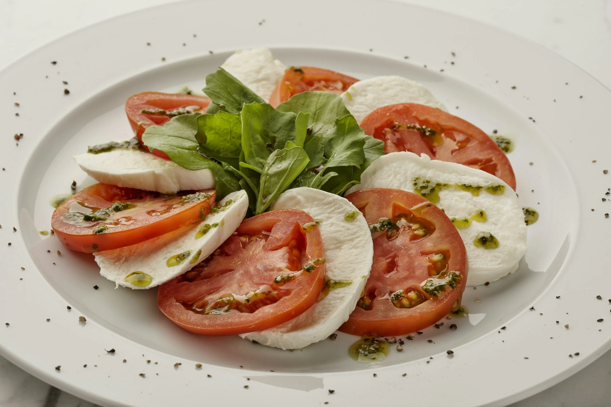 Caprese salad with slices of tomato, mozzarella cheese, fresh basil leaves, drizzled with olive oil and sprinkled with black pepper.