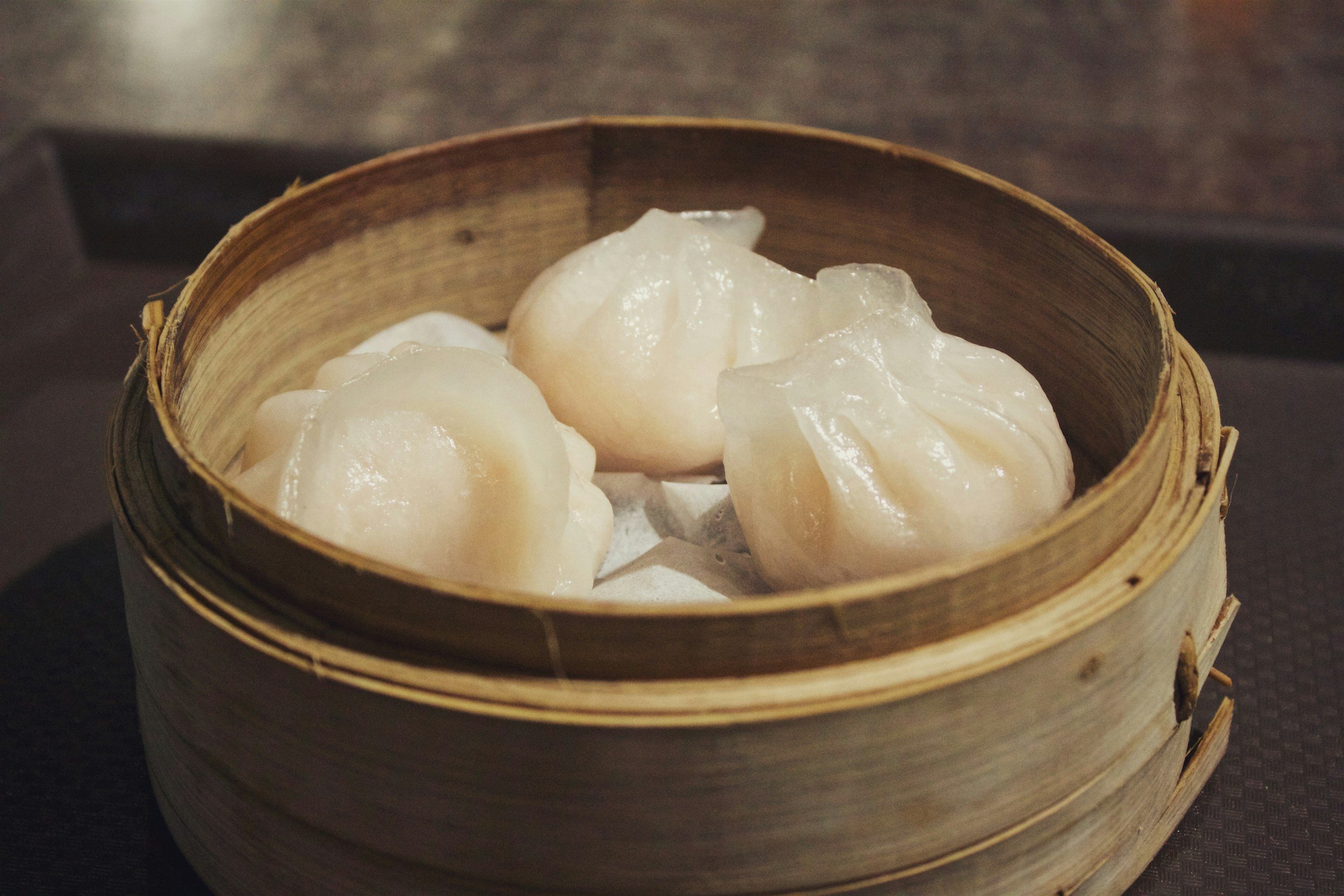 Four steamed shrimp dumplings in a traditional bamboo steamer basket.