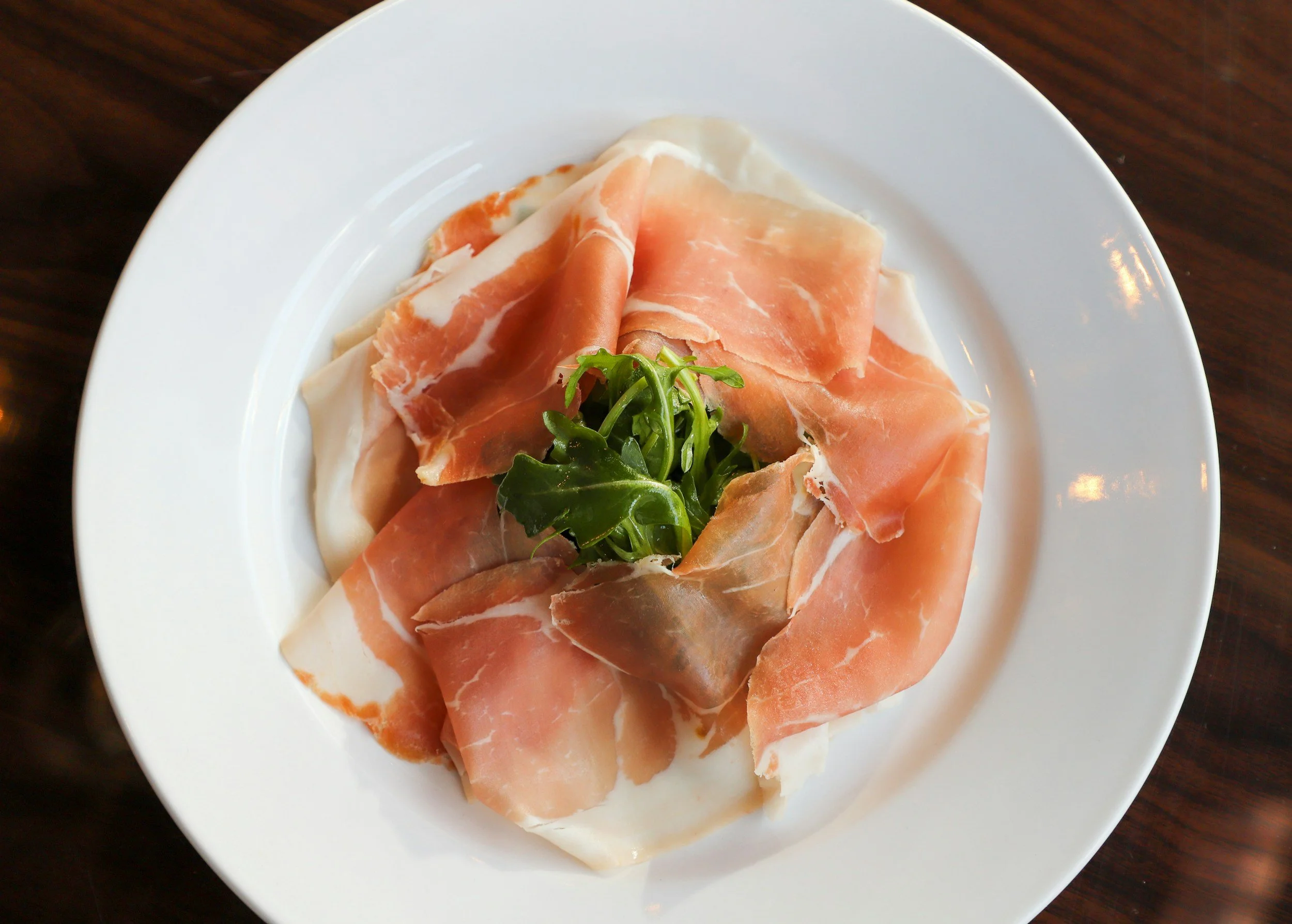 A white plate with slices of prosciutto ham and a small garnish of mixed greens in the center.