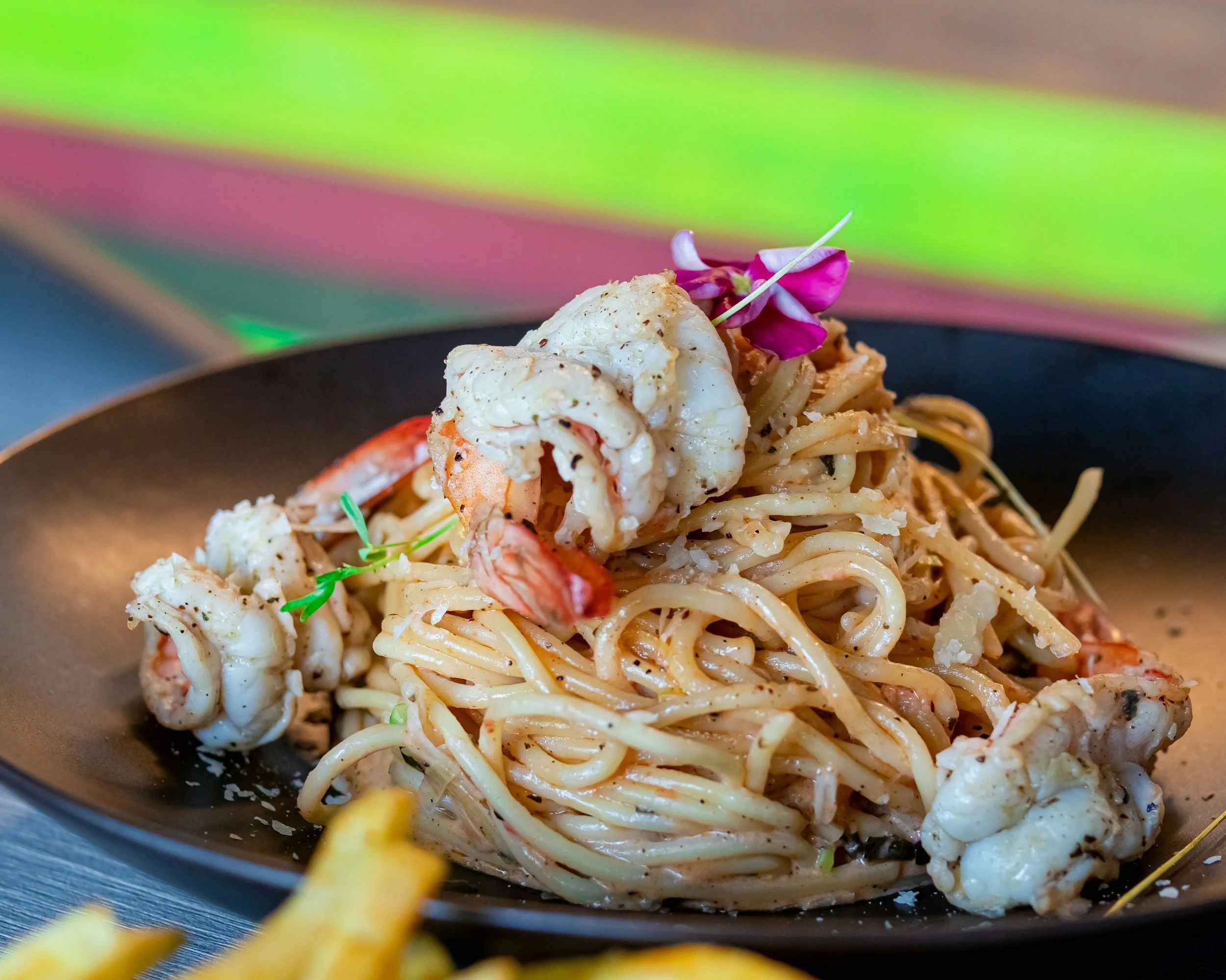 A plate of shrimp pasta garnished with a purple flower and green herbs.