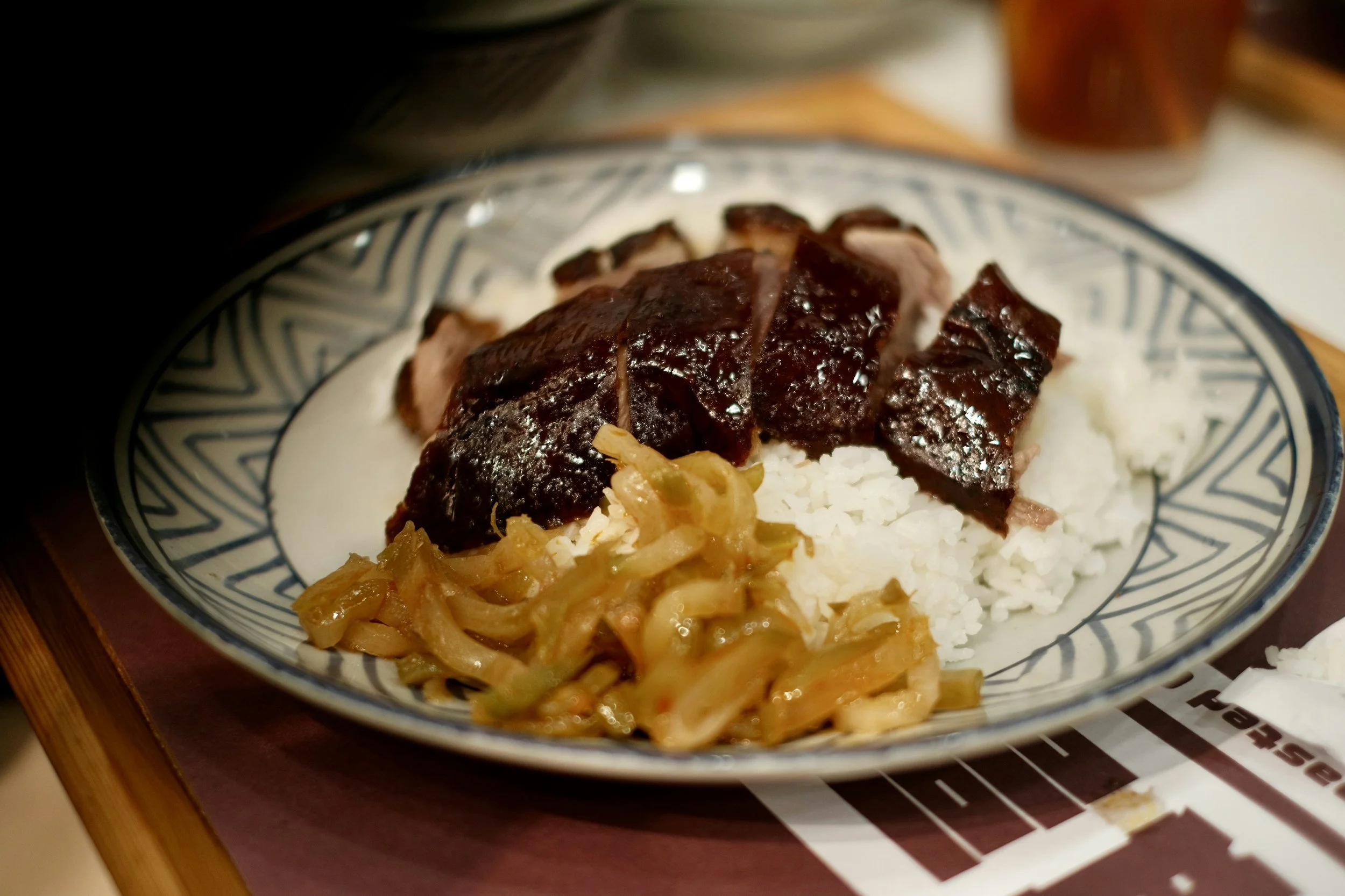 Plate of roasted pork with rice, pickled vegetables, and sauce.